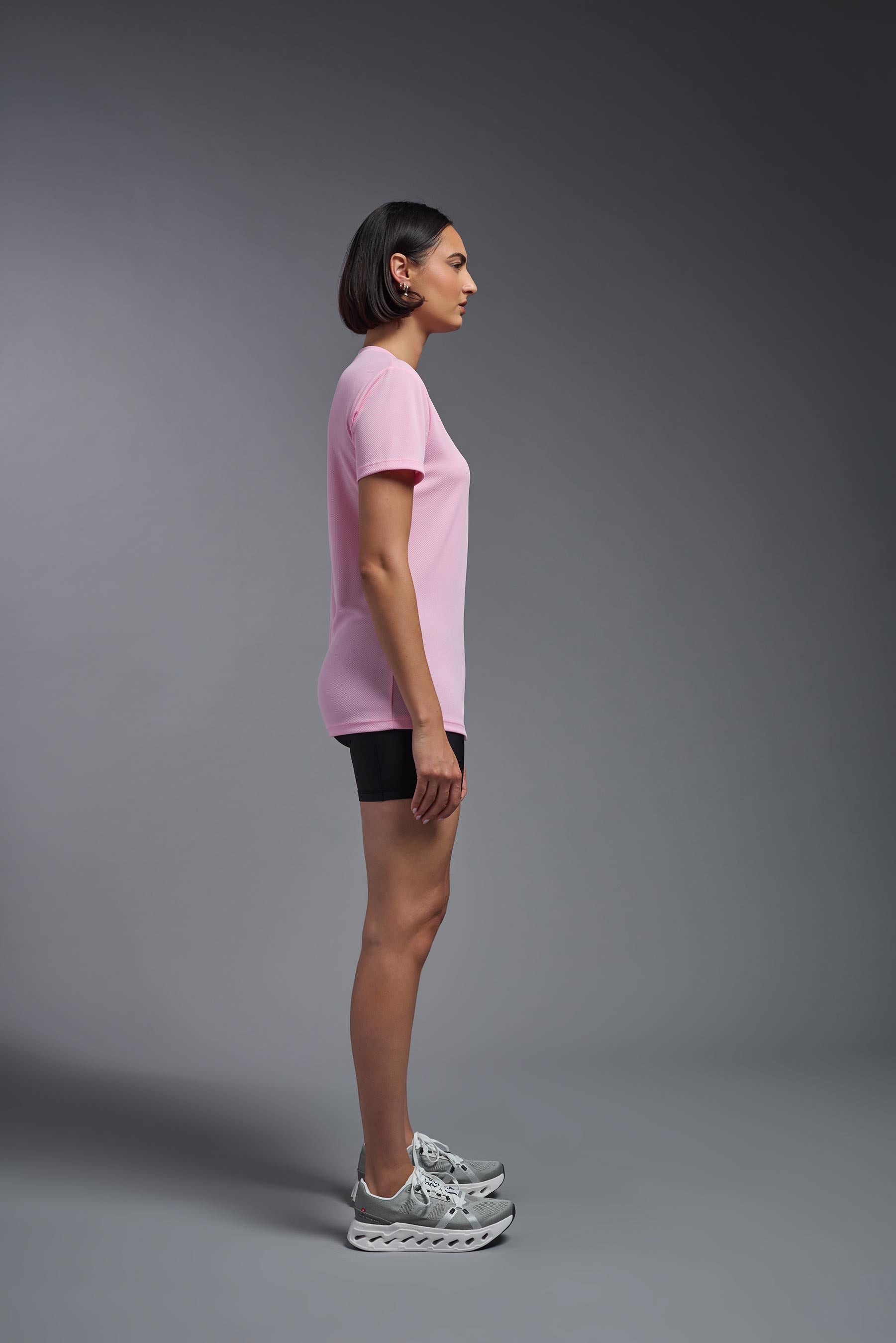 A female model wearing the women's Oxymesh V-neck Tech Tee in the color pink, made out of 100% polyester, showing the relaxed fit from a side view. This shirt is breathable, wicks away moisture, quick-dries, and is made in the USA. #pink