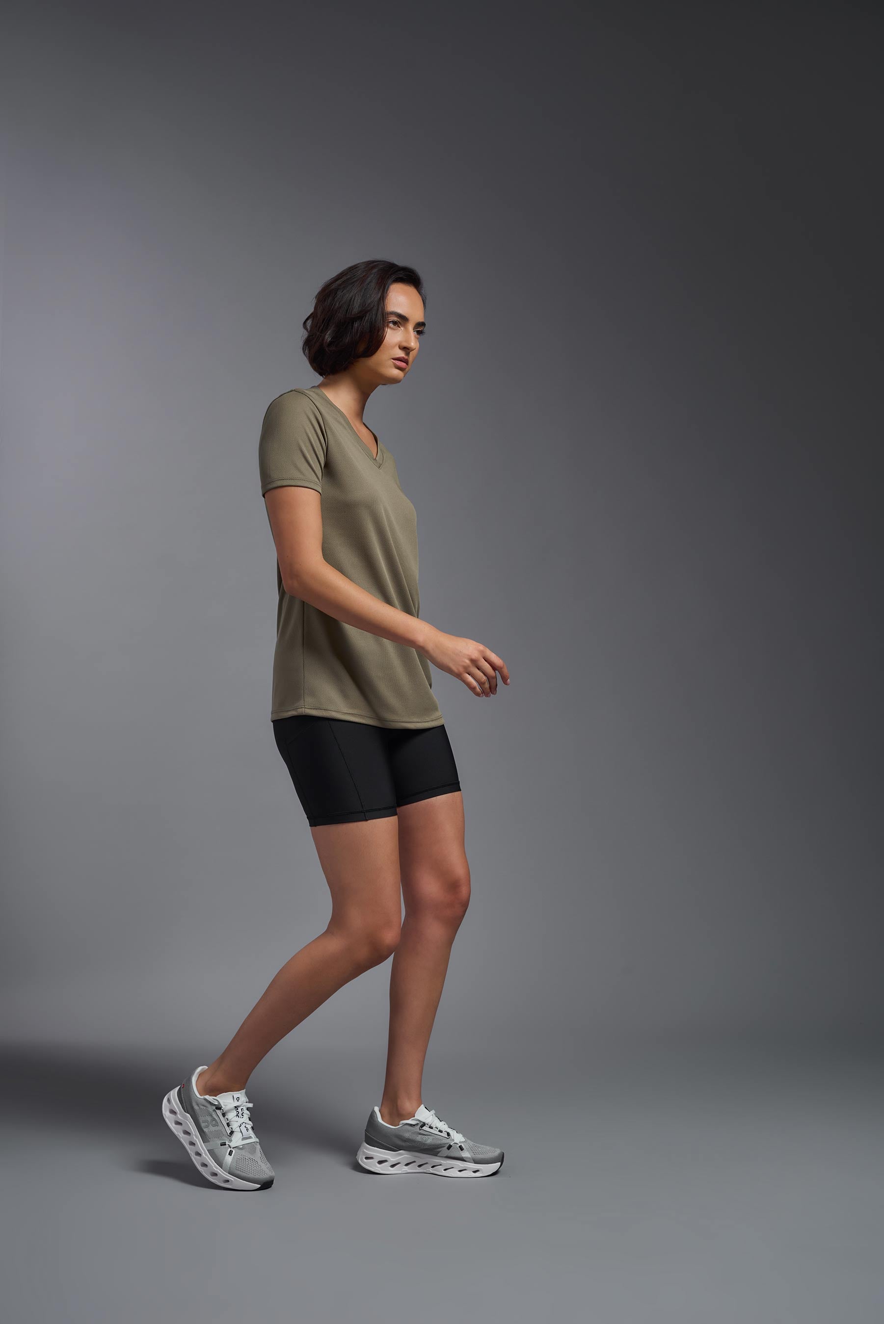 A female model wearing the women's Oxymesh V-neck Tech Tee in the color tan, made out of 100% polyester, showing the relaxed fit from a side view. This shirt is breathable, wicks away moisture, quick-dries, and is made in the USA. #tan
