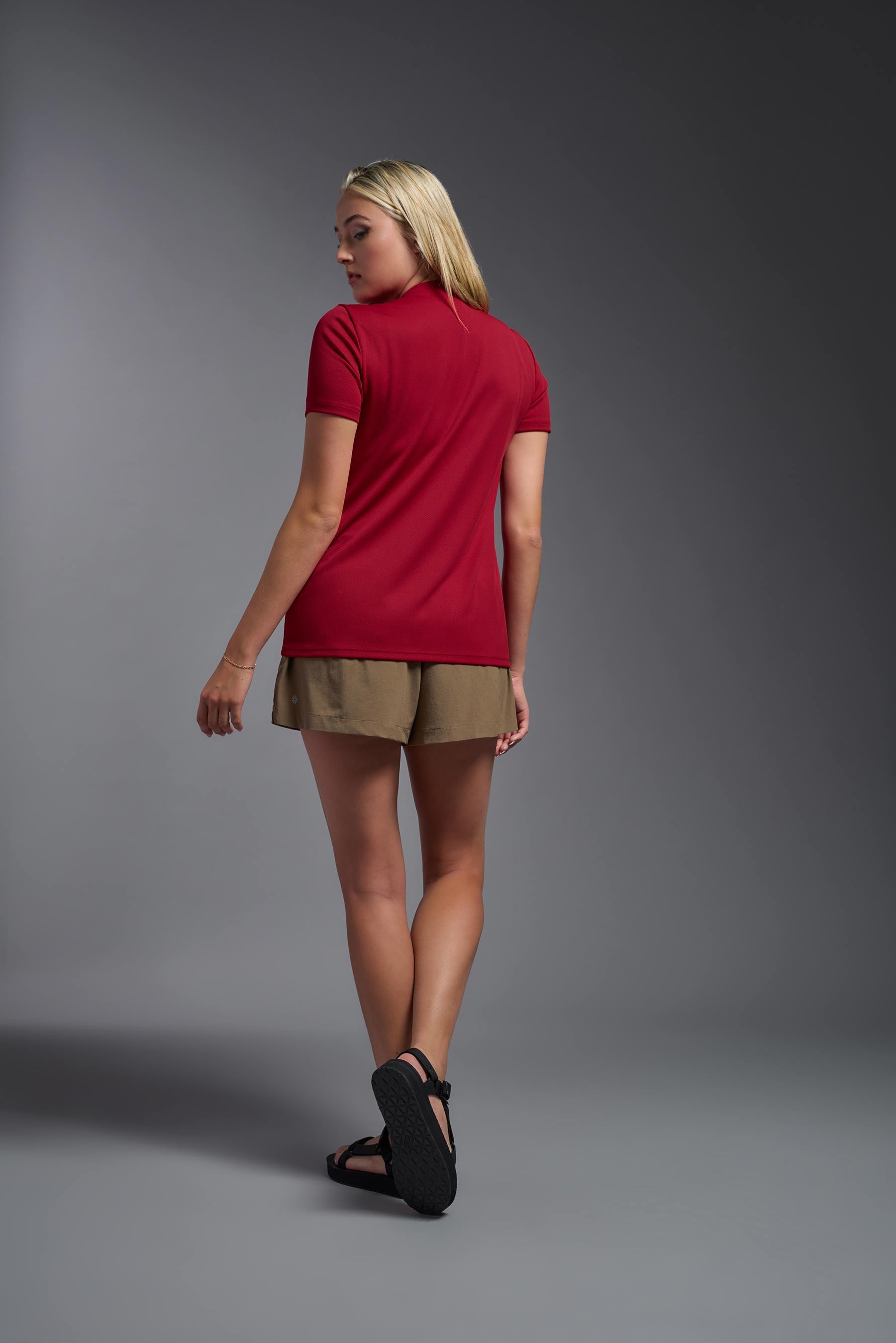 A female model wearing the women's Oxymesh V-neck Tech Tee in the color true red, made out of 100% polyester, showing the relaxed fit from a back view. This shirt is breathable, wicks away moisture, quick-dries, and is made in the USA. #true-red