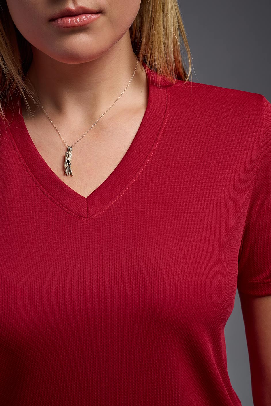 A female model wearing the women's Oxymesh V-neck Tech Tee in the color true red, made out of 100% polyester, showing the relaxed fit from a close-up collar view. This shirt is breathable, wicks away moisture, quick-dries, and is made in the USA. #true-red