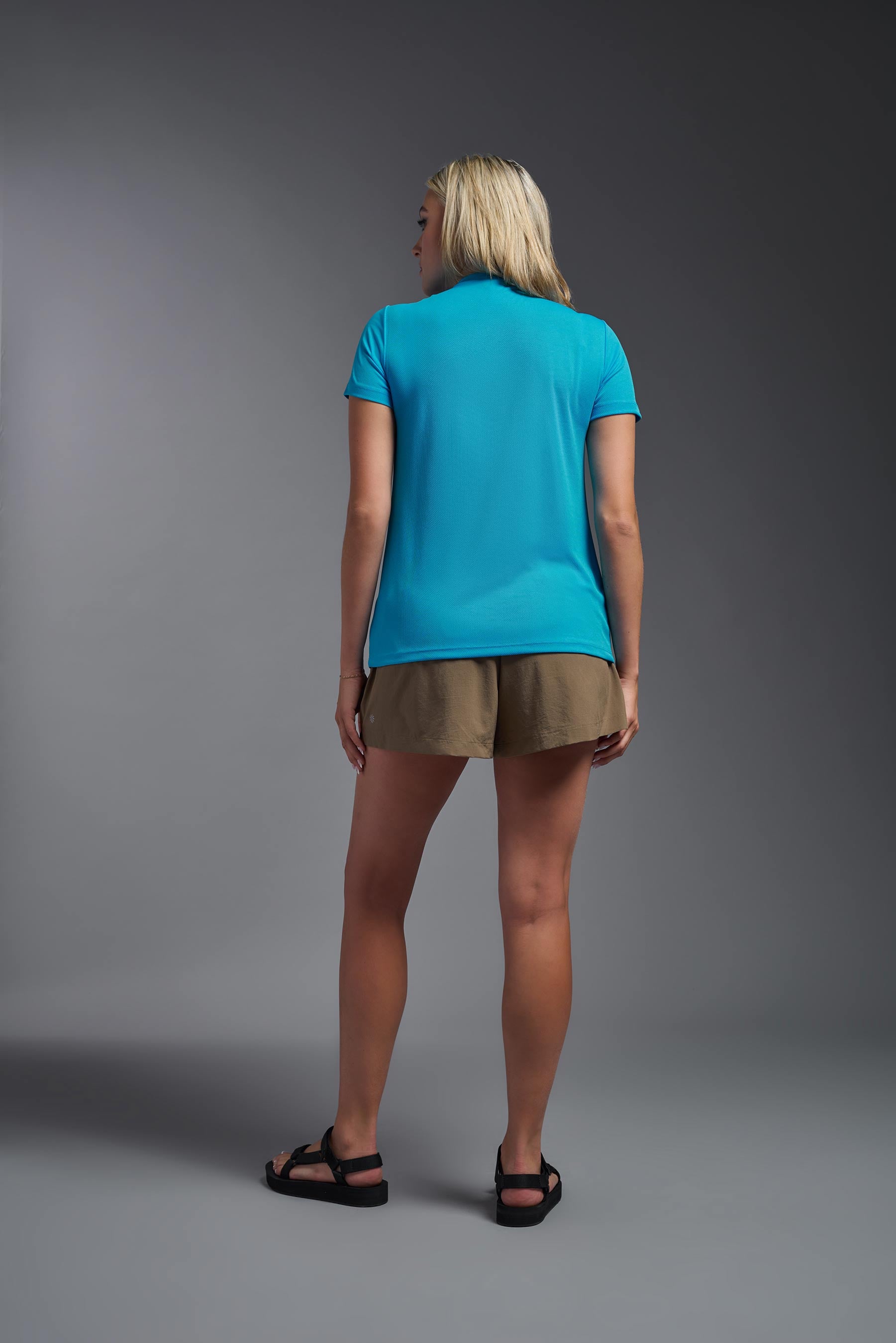 A female model wearing the women's Oxymesh V-neck Tech Tee in the color turquoise, made out of 100% polyester, showing the relaxed fit from a back view. This shirt is breathable, wicks away moisture, quick-dries, and is made in the USA. #turquoise