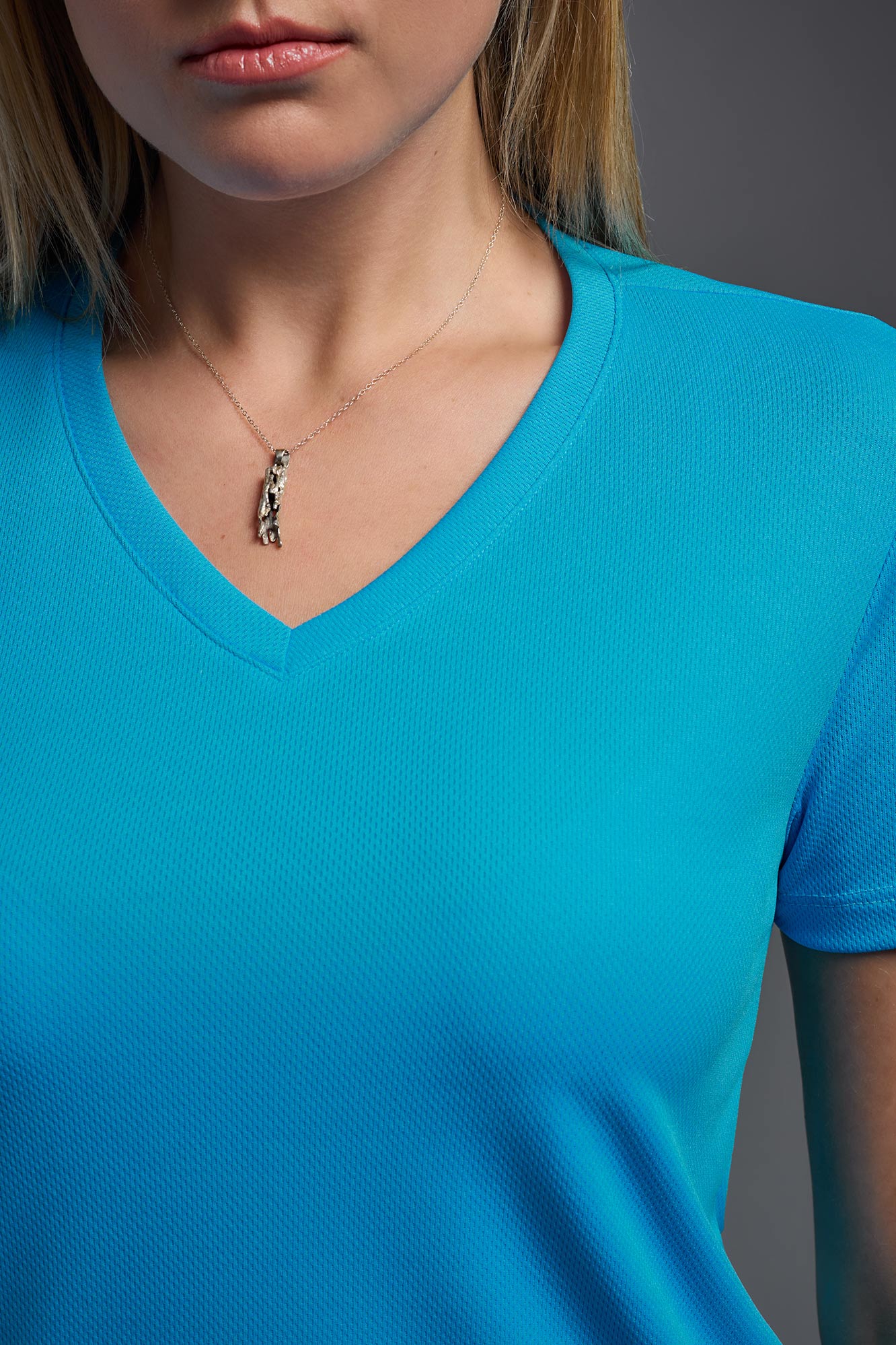 A female model wearing the women's Oxymesh V-neck Tech Tee in the color turquoise, made out of 100% polyester, showing the relaxed fit from a close-up collar view. This shirt is breathable, wicks away moisture, quick-dries, and is made in the USA. #turquoise