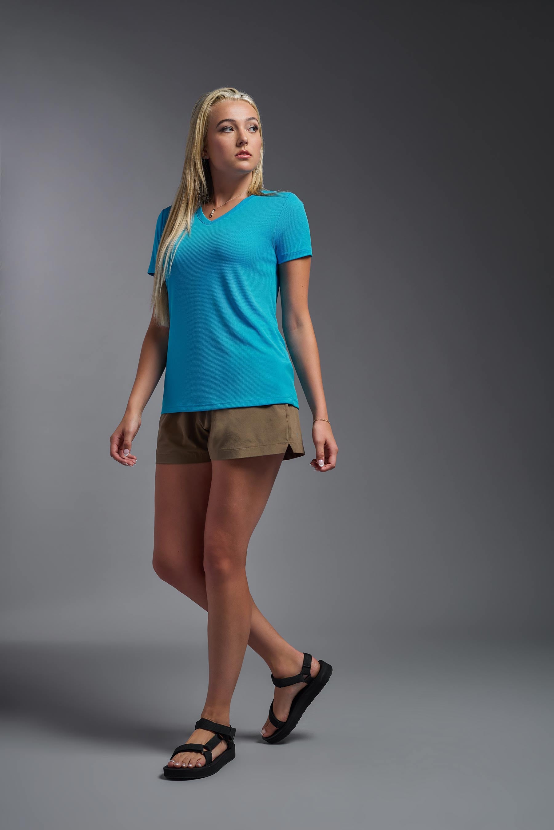 A female model wearing the women's Oxymesh V-neck Tech Tee in the color turquoise, made out of 100% polyester, showing the relaxed fit from a side view. This shirt is breathable, wicks away moisture, quick-dries, and is made in the USA. #turquoise