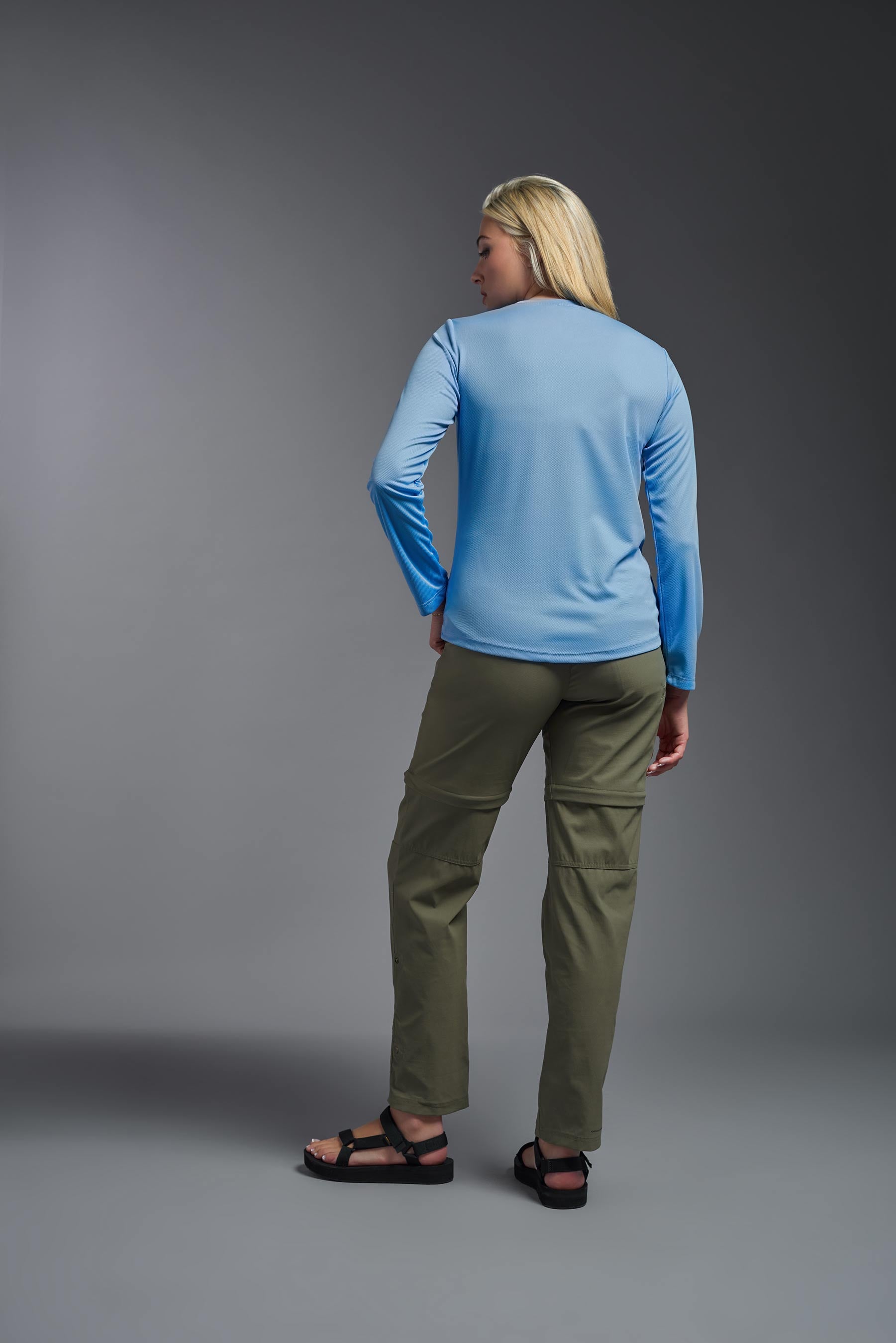A female model wearing the women's Oxymesh Long Sleeve Tech Tee Imported Version in the color carolina blue, made out of 100% polyester, showing the relaxed fit from a back view. This shirt is breathable, quick-drying, moisture-wicking, and Imported for a better price on bulk apparel. #carolina-blue