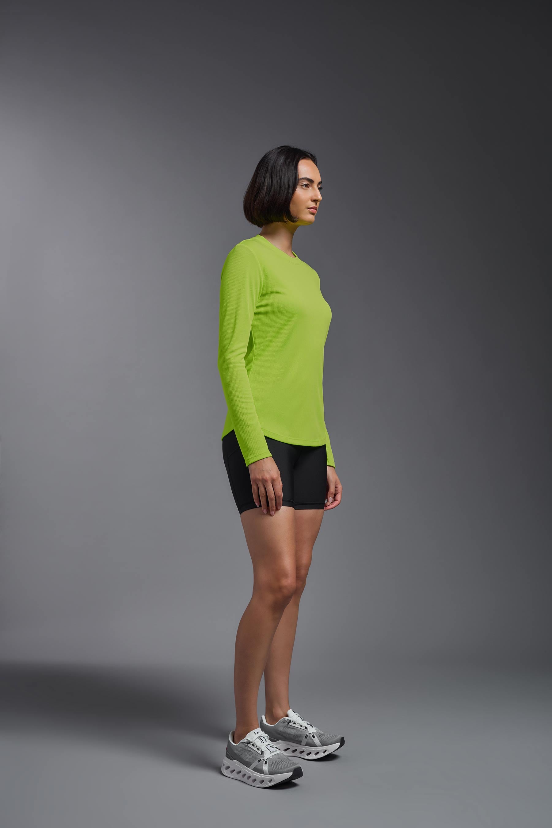 A female model wearing the women's Oxymesh Long Sleeve Tech Tee Imported Version in the color key lime, made out of 100% polyester, showing the relaxed fit from a side view. This shirt is breathable, quick-drying, moisture-wicking, and Imported for a better price on bulk apparel. #key-lime