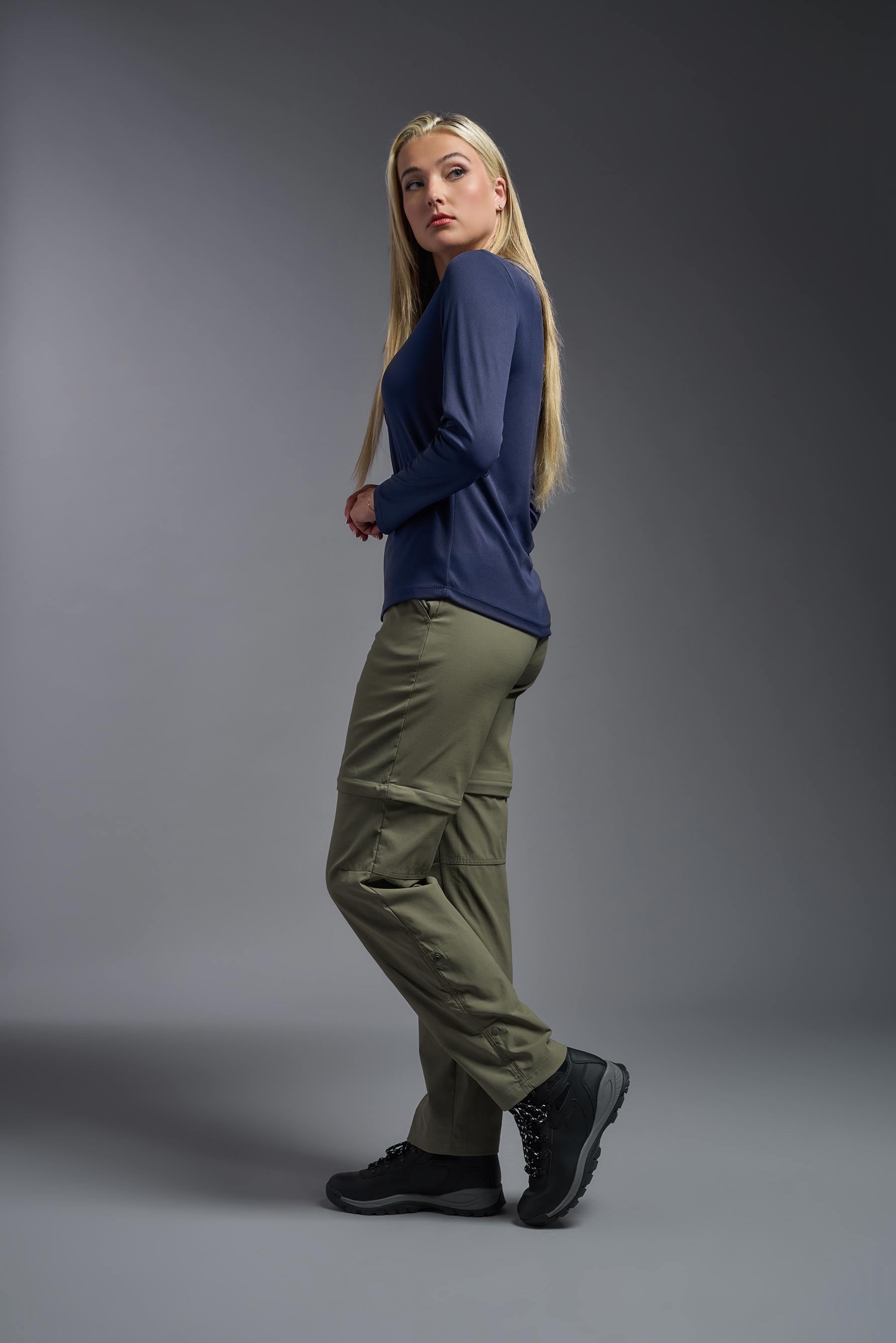 A female model wearing the women's Oxymesh Long Sleeve Tech Tee Imported Version in the color navy blue, made out of 100% polyester, showing the relaxed fit from a side view. This shirt is breathable, quick-drying, moisture-wicking, and Imported for a better price on bulk apparel. #navy-blue