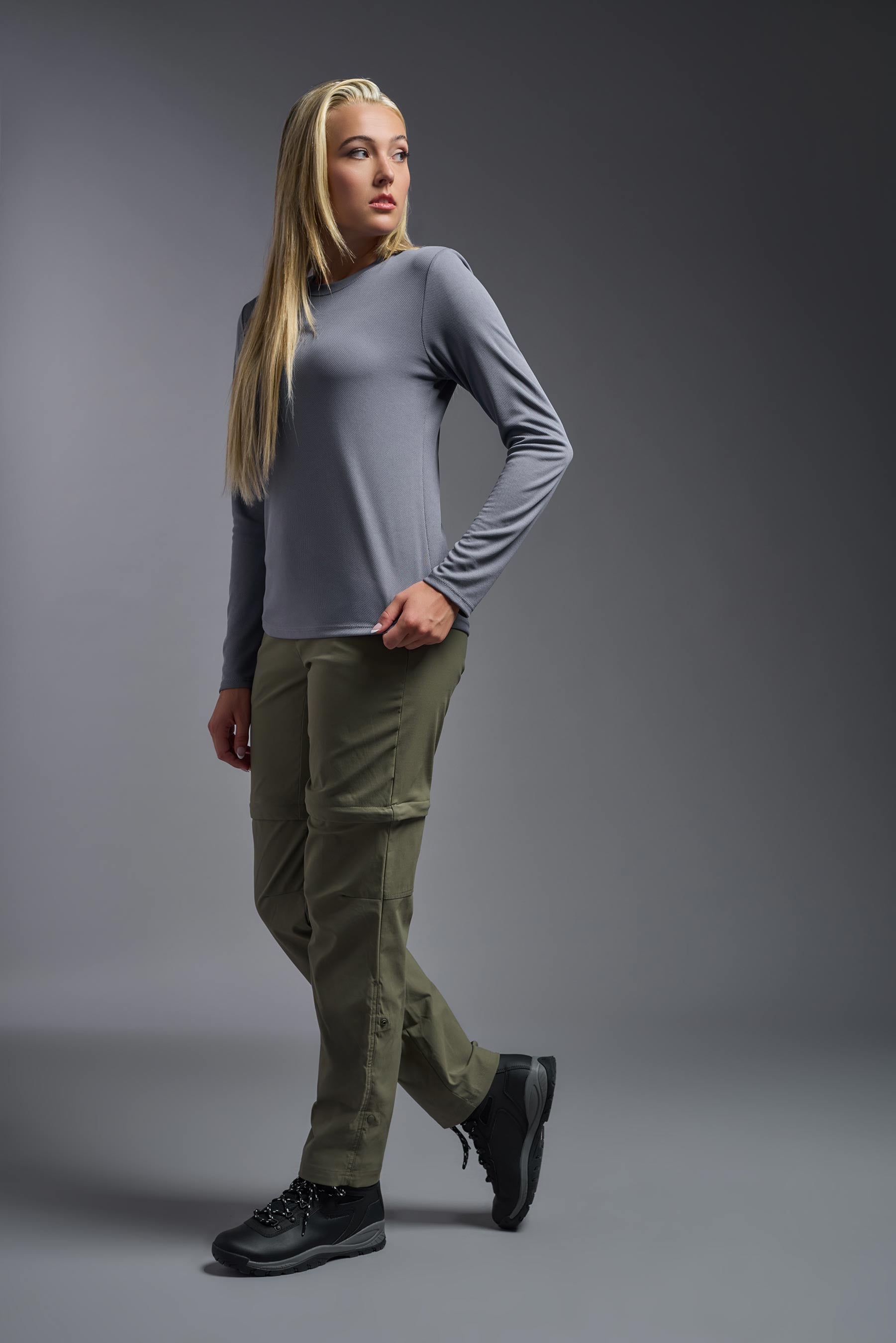 A female model wearing the women's Oxymesh Long Sleeve Tech Tee Imported Version in the color steel gray, made out of 100% polyester, showing the relaxed fit from a side view. This shirt is breathable, quick-drying, moisture-wicking, and Imported for a better price on bulk apparel. #steel-gray