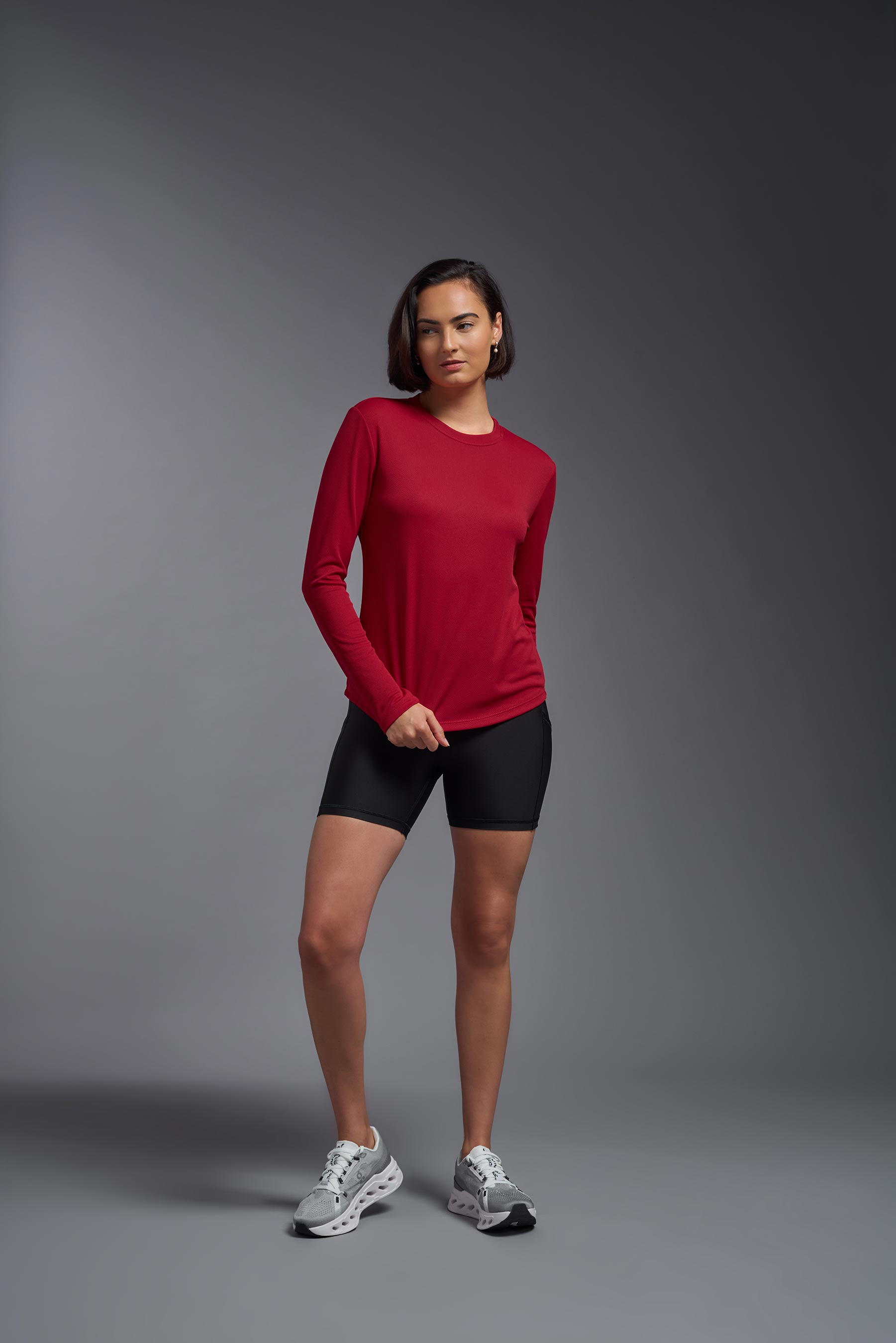 A female model wearing the women's Oxymesh Long Sleeve Tech Tee Imported Version in the color true red, made out of 100% polyester, showing the relaxed fit from a front view. This shirt is breathable, quick-drying, moisture-wicking, and Imported for a better price on bulk apparel. #true-red