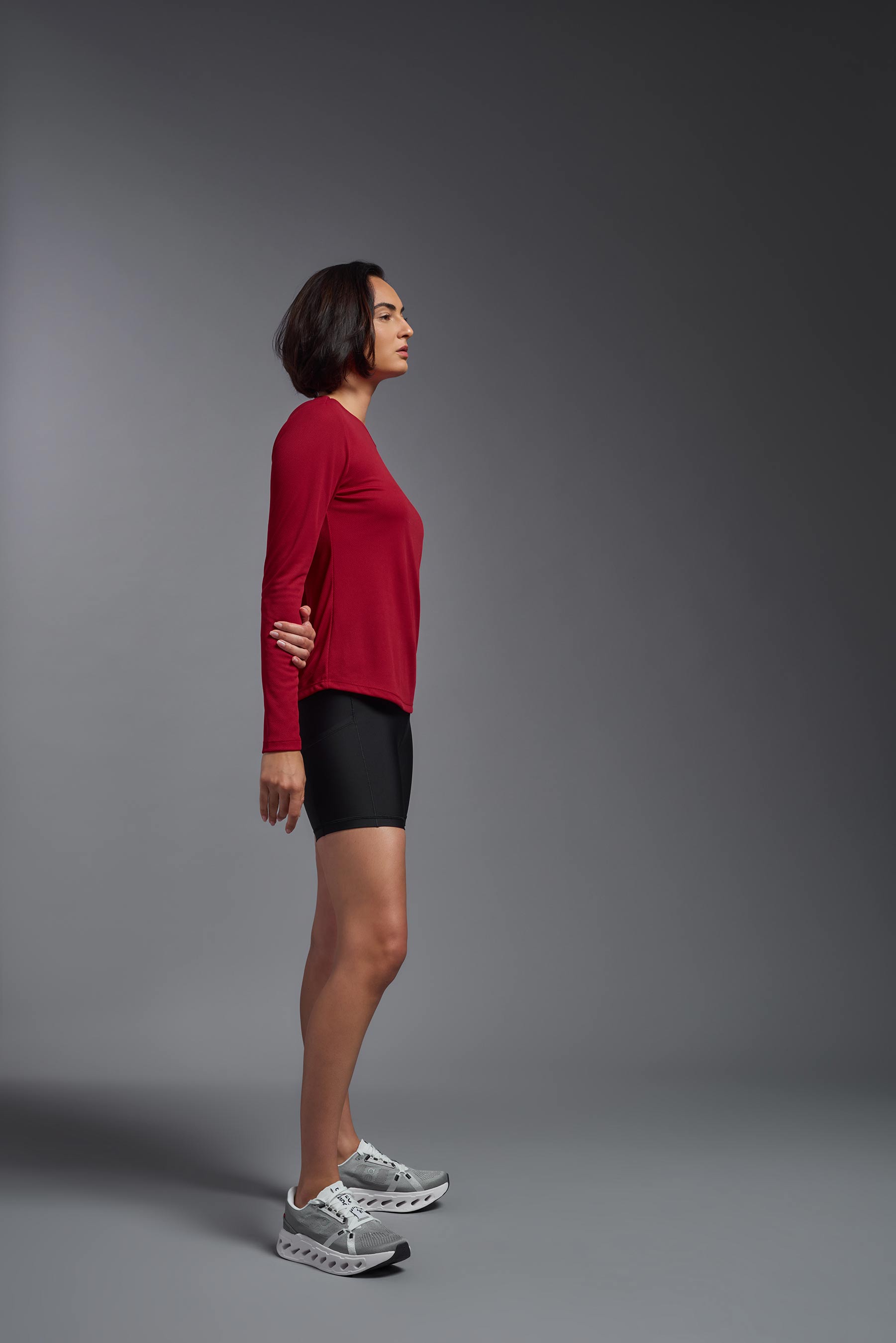 A female model wearing the women's Oxymesh Long Sleeve Tech Tee Imported Version in the color true red, made out of 100% polyester, showing the relaxed fit from a side view. This shirt is breathable, quick-drying, moisture-wicking, and Imported for a better price on bulk apparel. #true-red