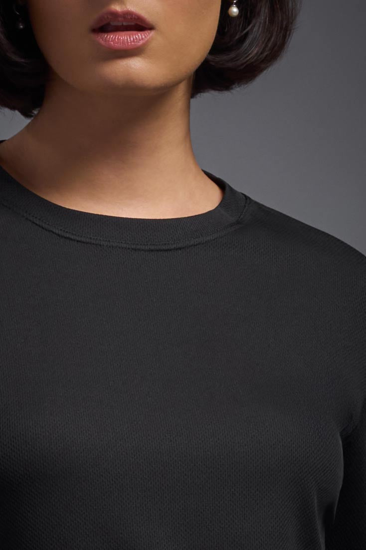 A female model wearing the women's Oxymesh Long Sleeve Tech Tee in the color black, made out of 100% polyester, showing the relaxed fit from a front collar close-up view. This shirt is breathable, quick-drying, moisture-wicking, and made in the USA. #black