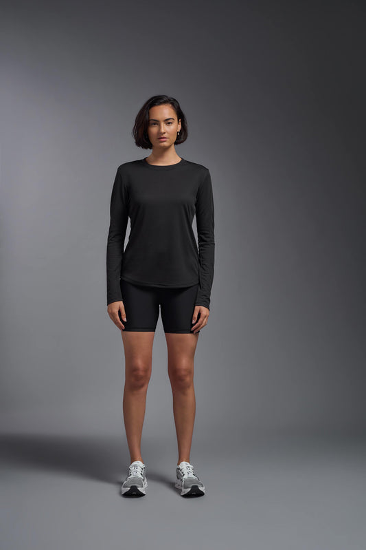 A female model wearing the women's Oxymesh Long Sleeve Tech Tee in the color black, made out of 100% polyester, showing the relaxed fit from a front view. This shirt is breathable, quick-drying, moisture-wicking, and made in the USA. #black