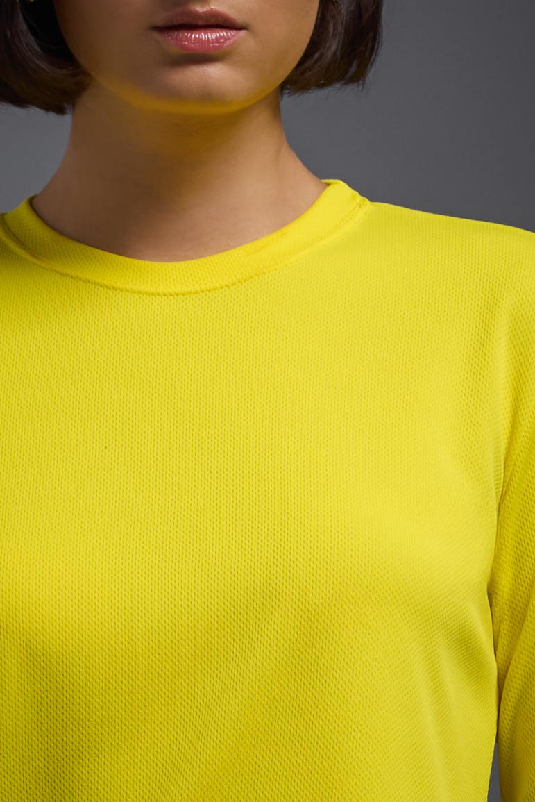 A female model wearing the women's Oxymesh Long Sleeve Tech Tee in the color bright yellow, made out of 100% polyester, showing the relaxed fit from a collar close-up view. This shirt is breathable, quick-drying, moisture-wicking, and made in the USA. #bright-yellow