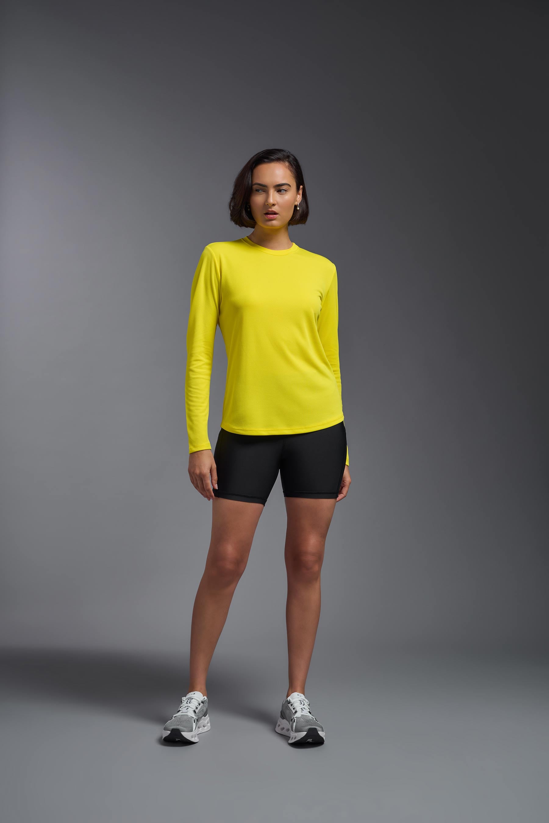 A female model wearing the women's Oxymesh Long Sleeve Tech Tee in the color bright yellow, made out of 100% polyester, showing the relaxed fit from a front view. This shirt is breathable, quick-drying, moisture-wicking, and made in the USA. #bright-yellow