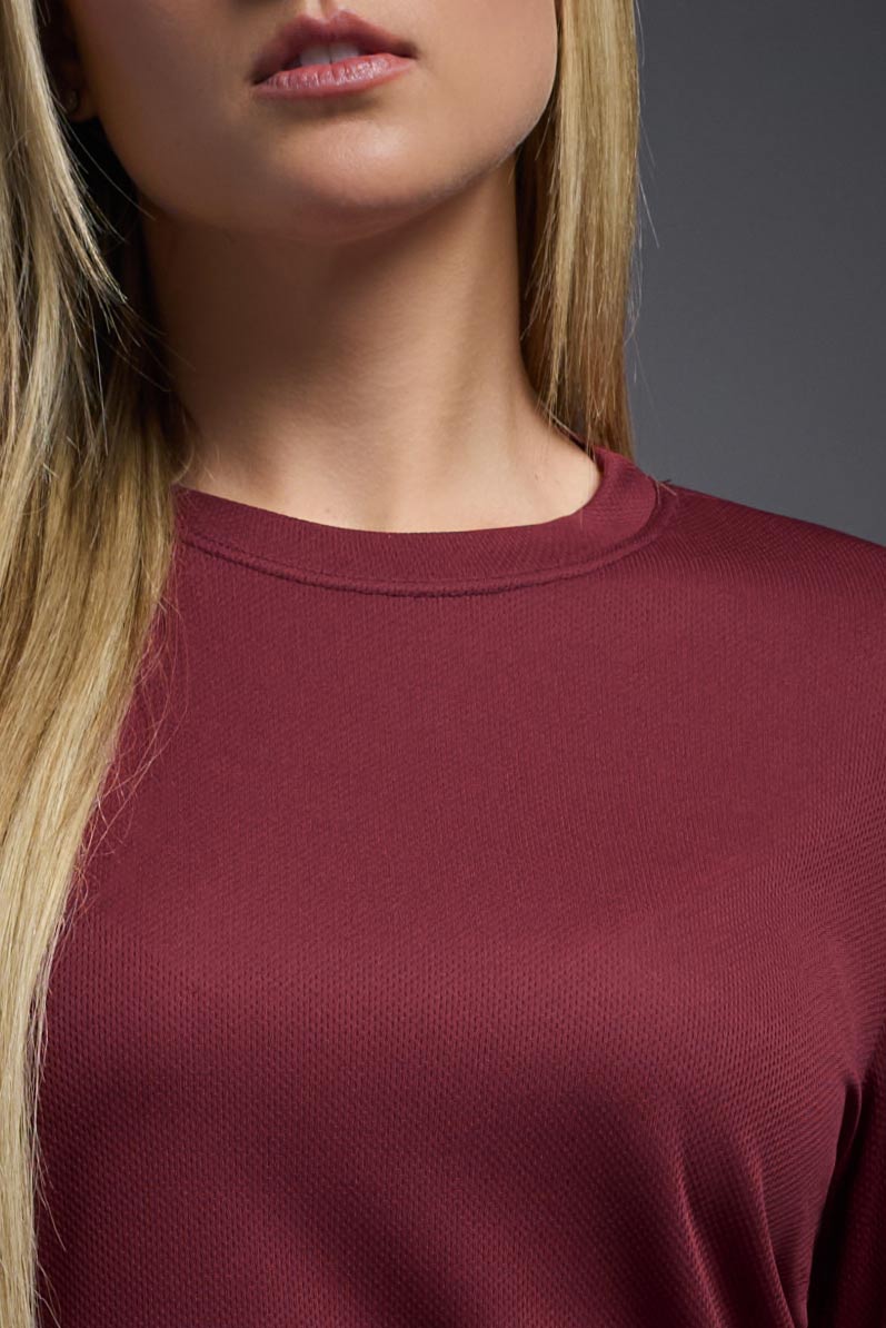 A female model wearing the women's Oxymesh Long Sleeve Tech Tee in the color cardinal, made out of 100% polyester, showing the relaxed fit from a front collar close-up view. This shirt is breathable, quick-drying, moisture-wicking, and made in the USA. #cardinal-red