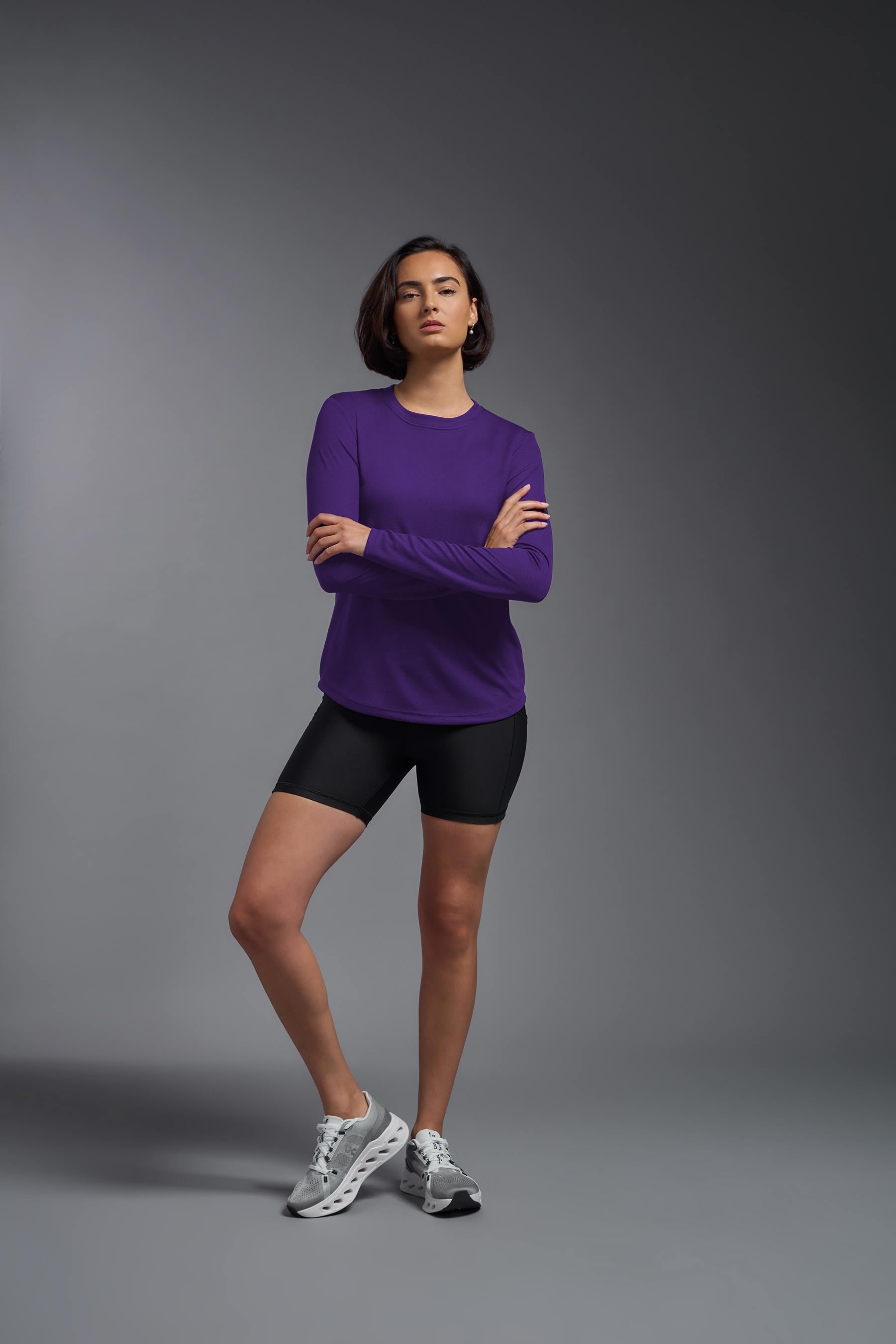 A female model wearing the women's Oxymesh Long Sleeve Tech Tee in the color dark purple, made out of 100% polyester, showing the relaxed fit from a front view. This shirt is breathable, quick-drying, moisture-wicking, and made in the USA. #dark-purple