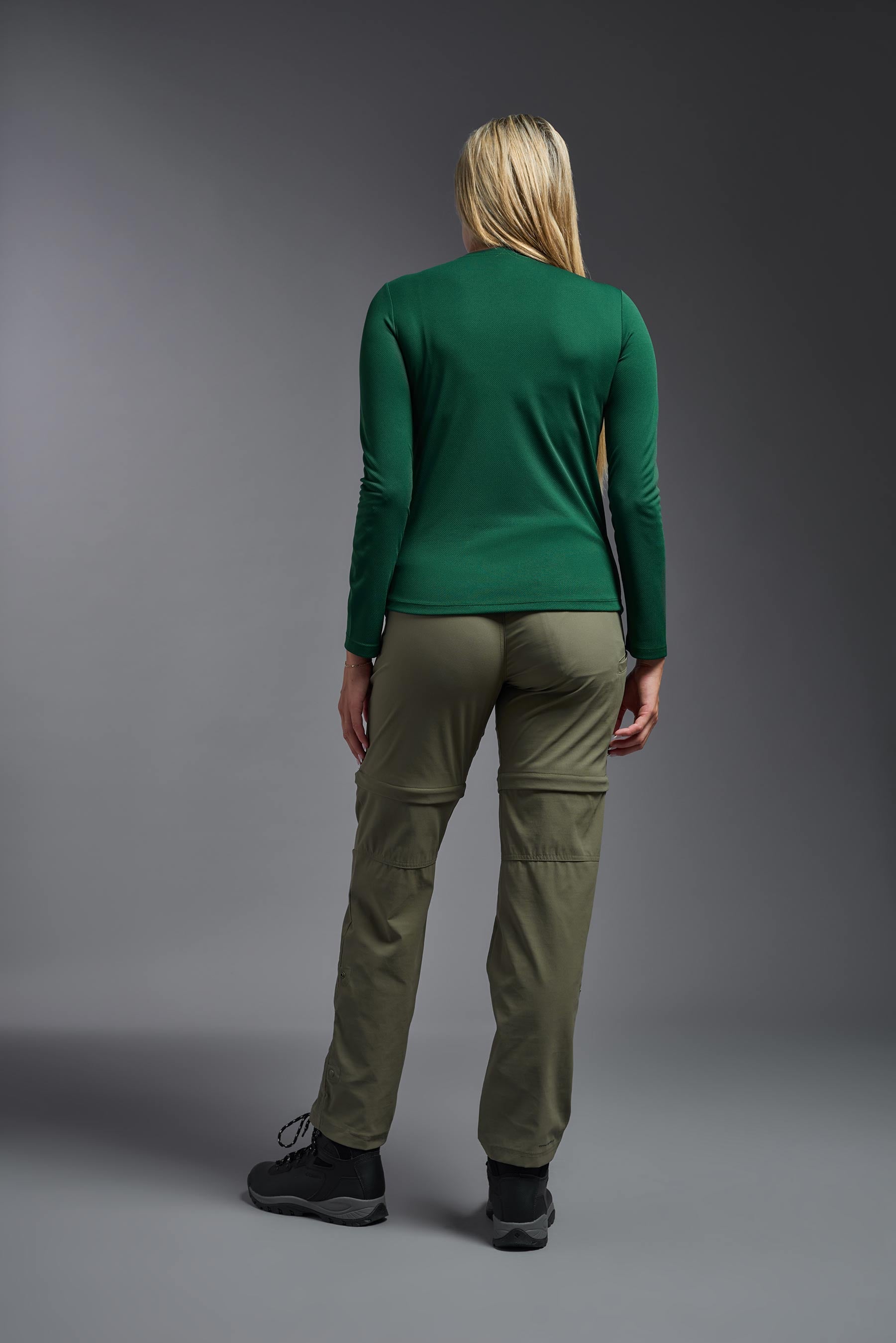 A female model wearing the women's Oxymesh Long Sleeve Tech Tee in the color forest green, made out of 100% polyester, showing the relaxed fit from a back view. This shirt is breathable, quick-drying, moisture-wicking, and made in the USA. #forest-green