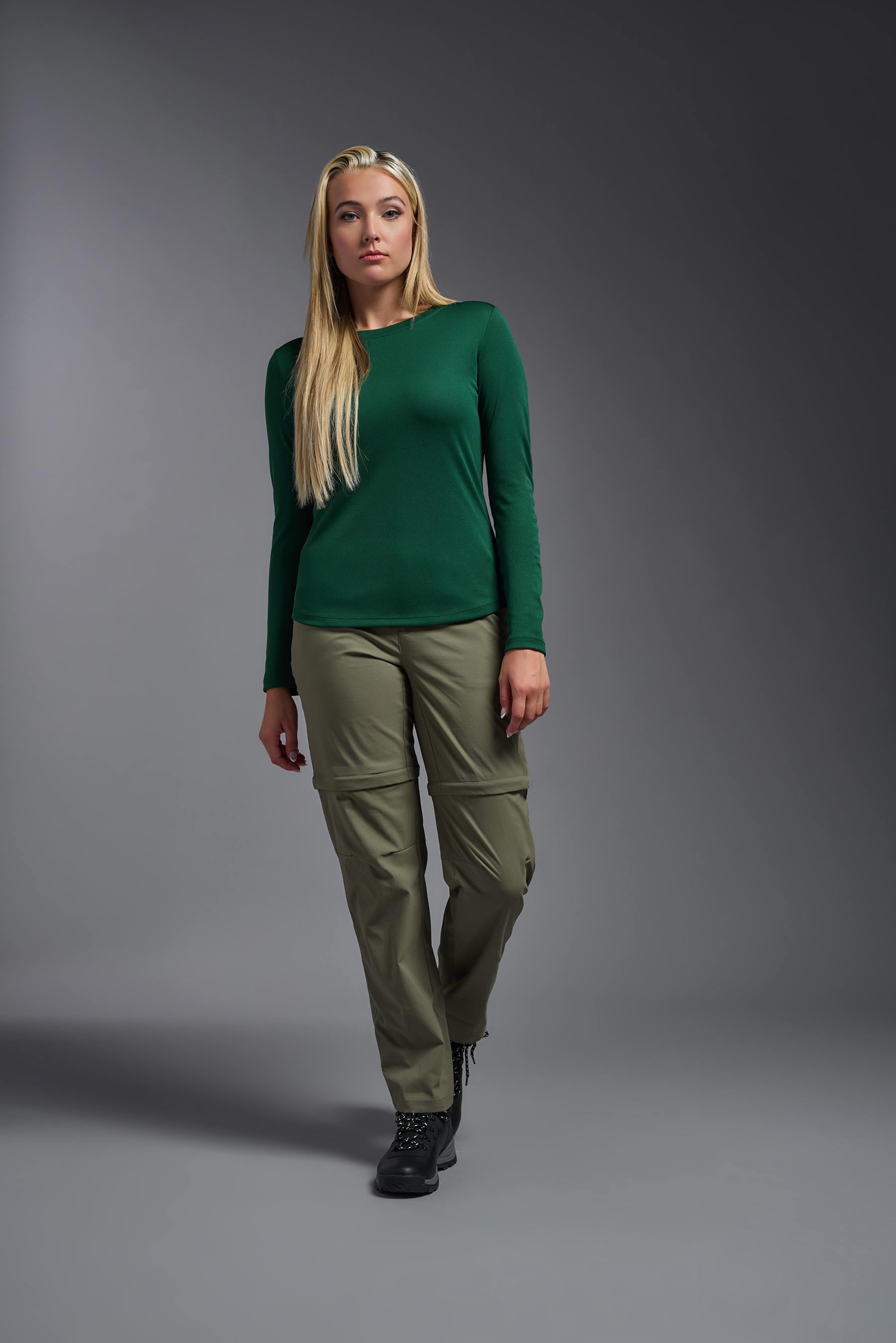A female model wearing the women's Oxymesh Long Sleeve Tech Tee in the color forest green, made out of 100% polyester, showing the relaxed fit from a front view. This shirt is breathable, quick-drying, moisture-wicking, and made in the USA. #forest-green