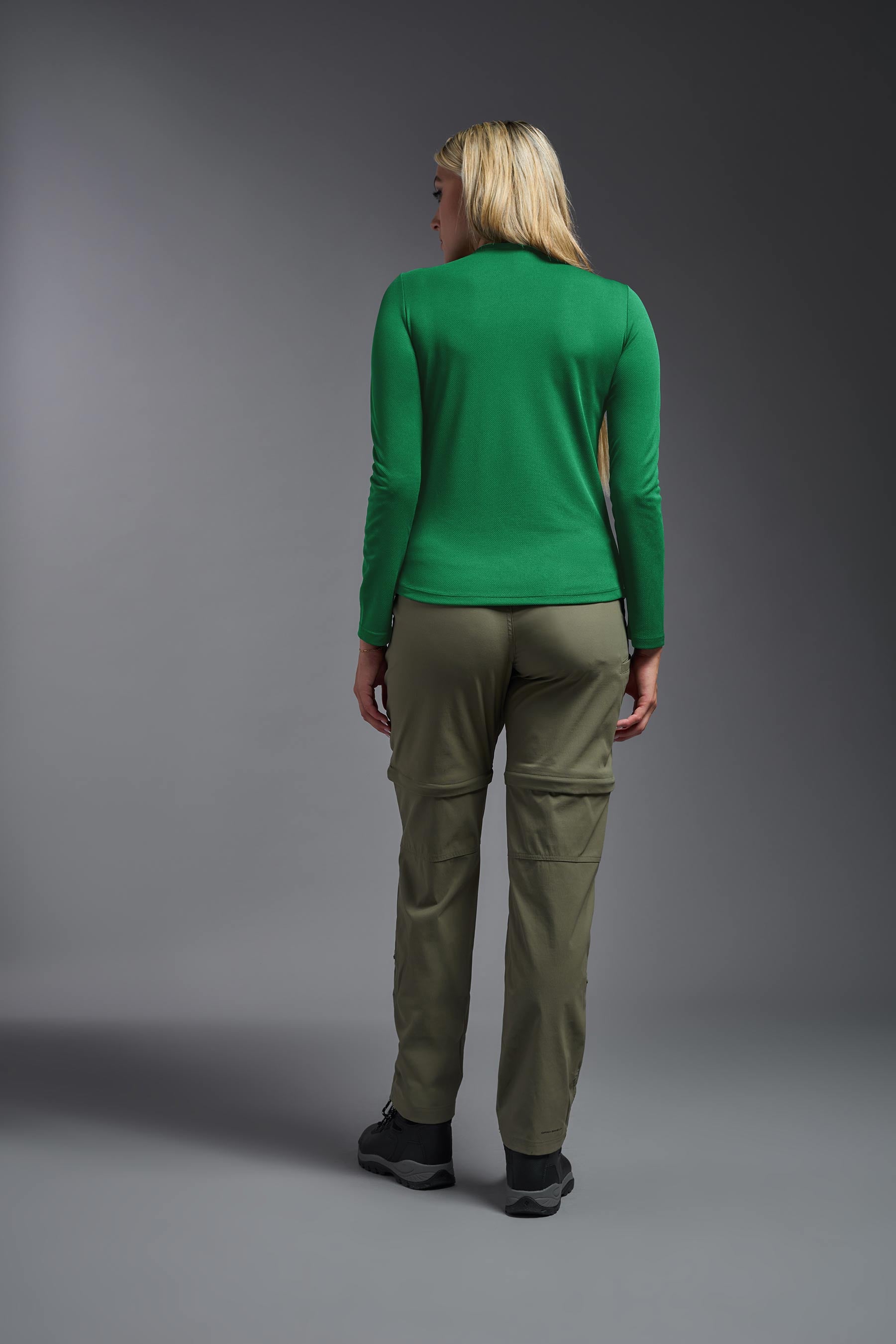 A female model wearing the women's Oxymesh Long Sleeve Tech Tee in the color kelly green, made out of 100% polyester, showing the relaxed fit from a back view. This shirt is breathable, quick-drying, moisture-wicking, and made in the USA. #kelly-green