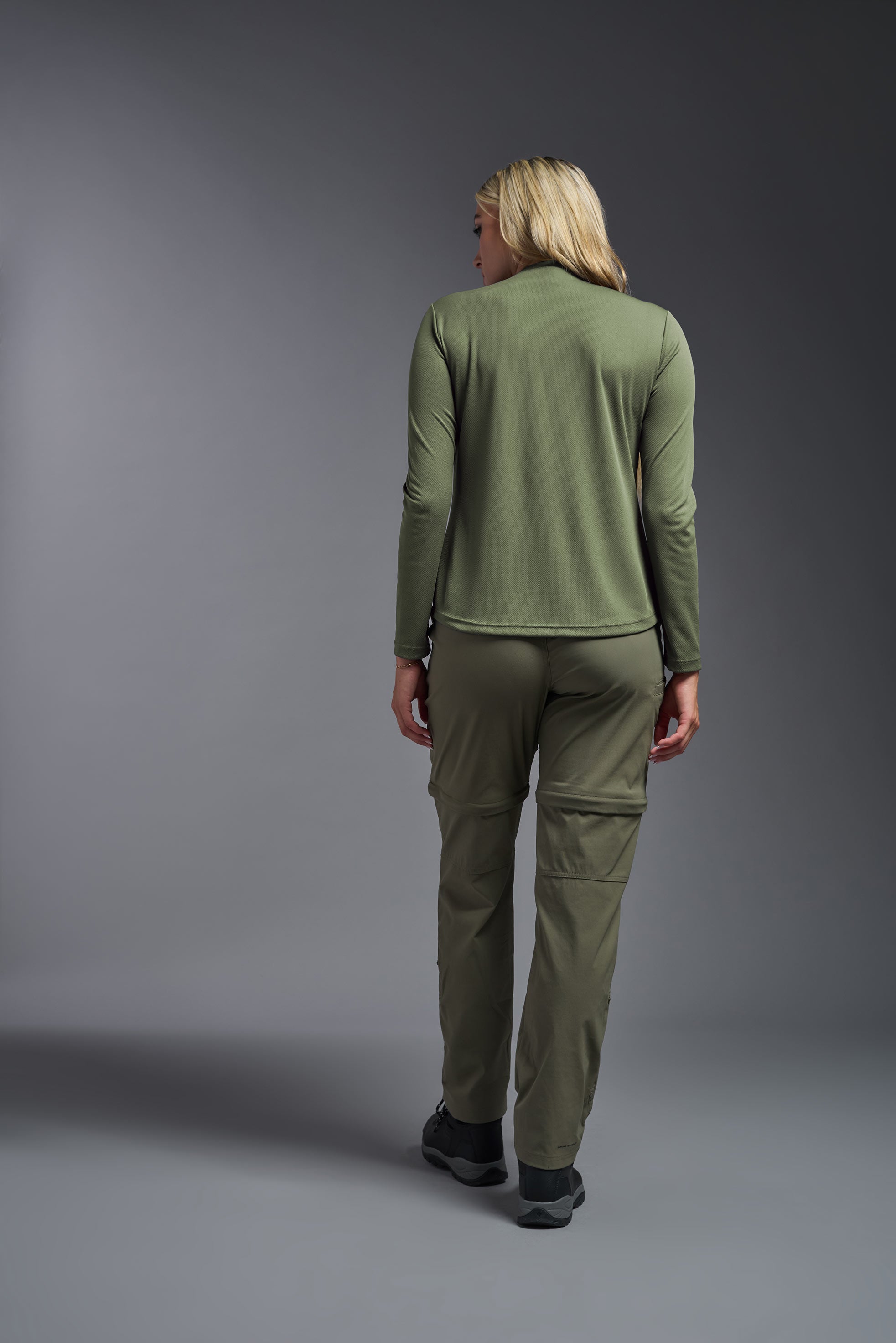 A female model wearing the women's Oxymesh Long Sleeve Tech Tee in the color military green, made out of 100% polyester, showing the relaxed fit from a back view. This shirt is breathable, quick-drying, moisture-wicking, and made in the USA. #military-green