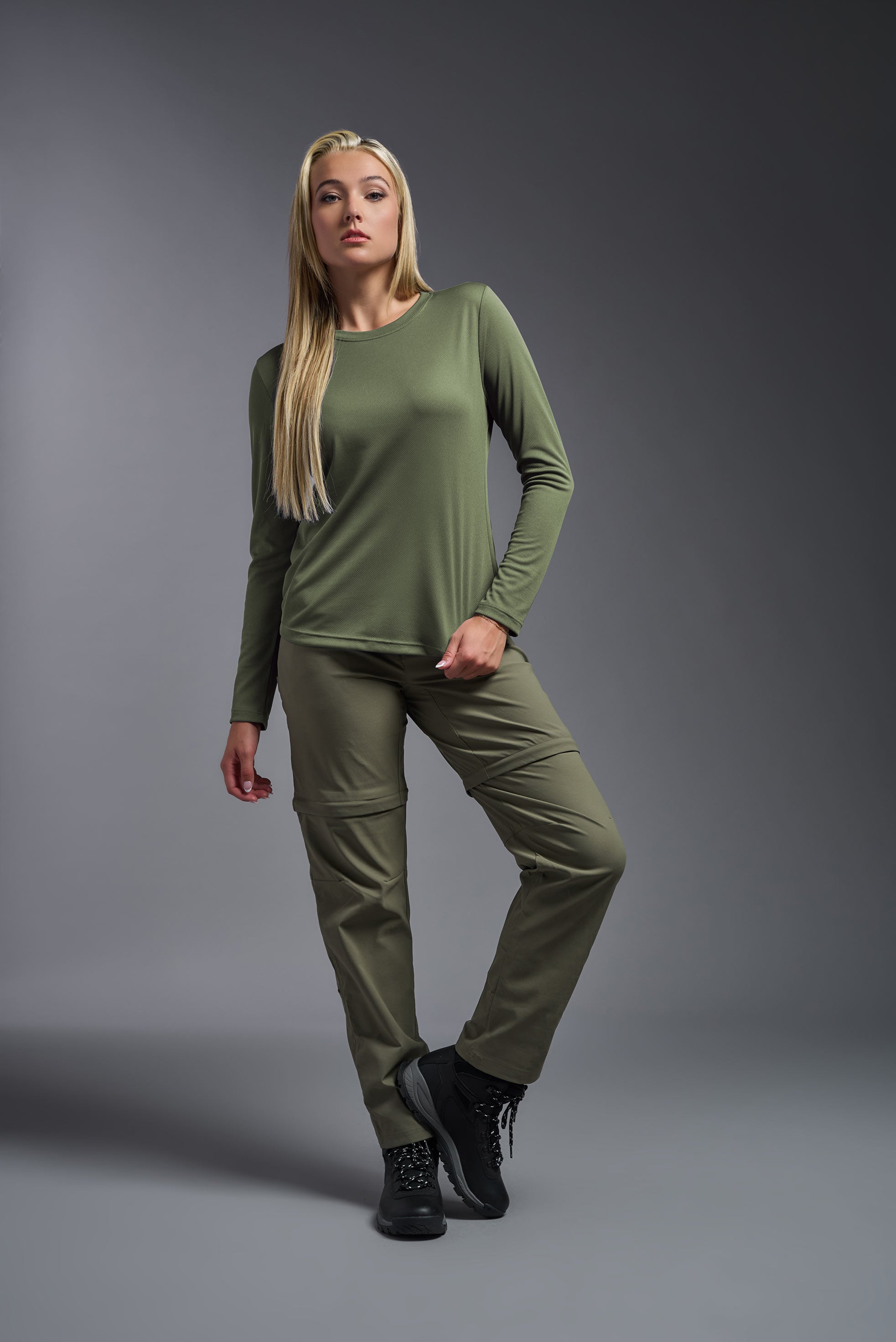 A female model wearing the women's Oxymesh Long Sleeve Tech Tee in the color military green, made out of 100% polyester, showing the relaxed fit from a front view. This shirt is breathable, quick-drying, moisture-wicking, and made in the USA. #military-green
