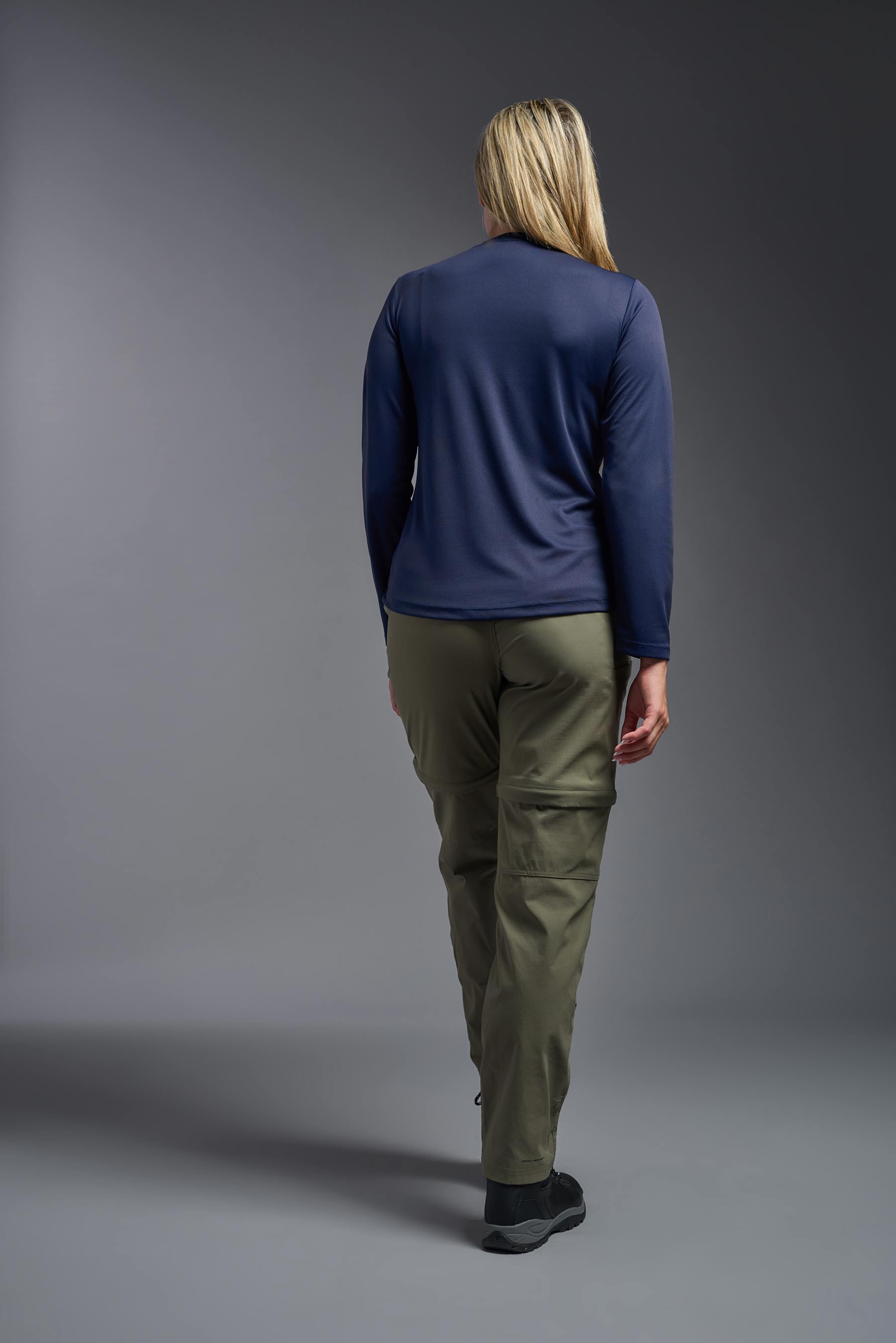 A female model wearing the women's Oxymesh Long Sleeve Tech Tee in the color navy, made out of 100% polyester, showing the relaxed fit from a back view. This shirt is breathable, quick-drying, moisture-wicking, and made in the USA. #navy