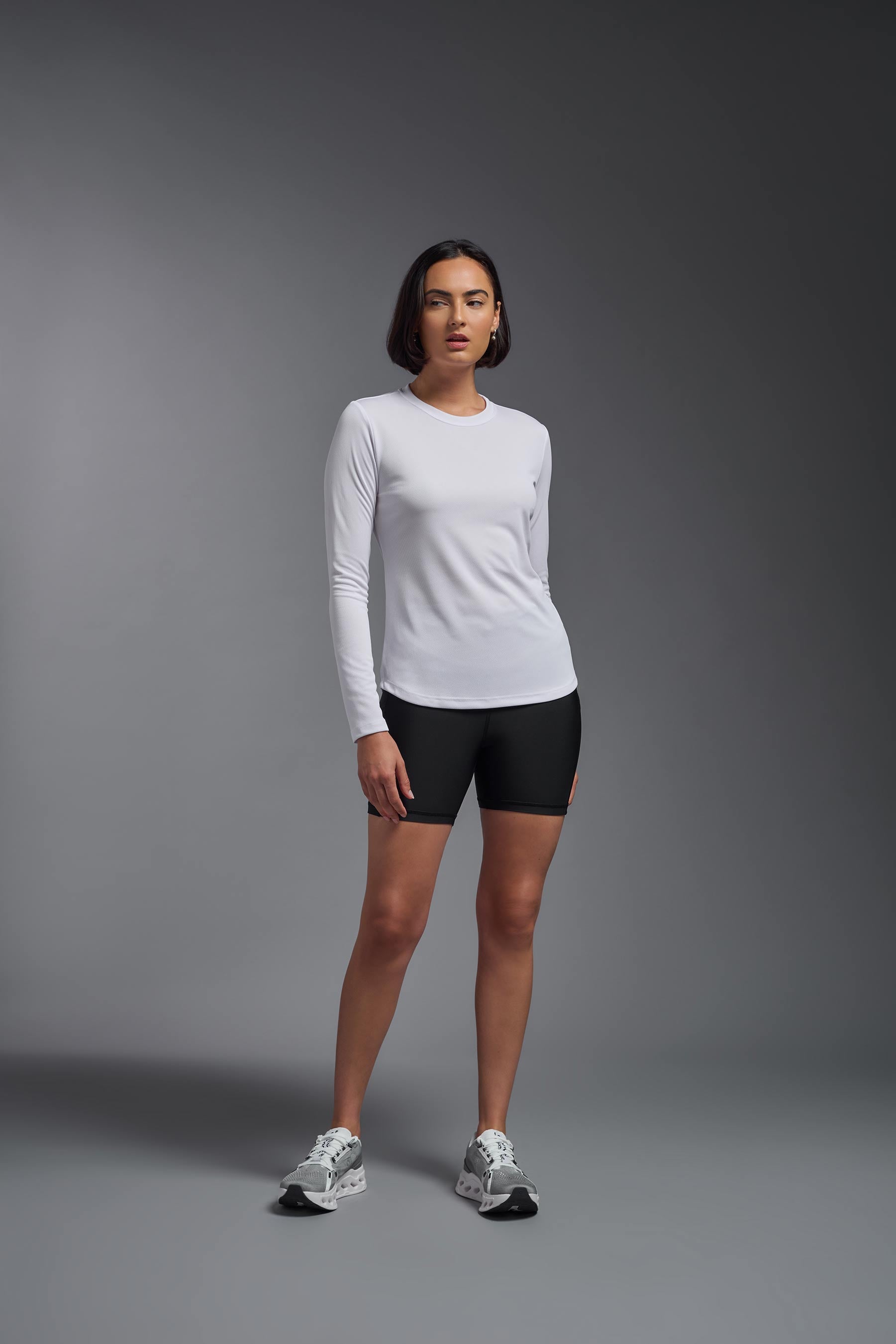 A female model wearing the women's Oxymesh Long Sleeve Tech Tee in the color white made out of 100% polyester, showing the relaxed fit from a front view. This shirt is breathable, quick-drying, moisture-wicking, and made in the USA. #white