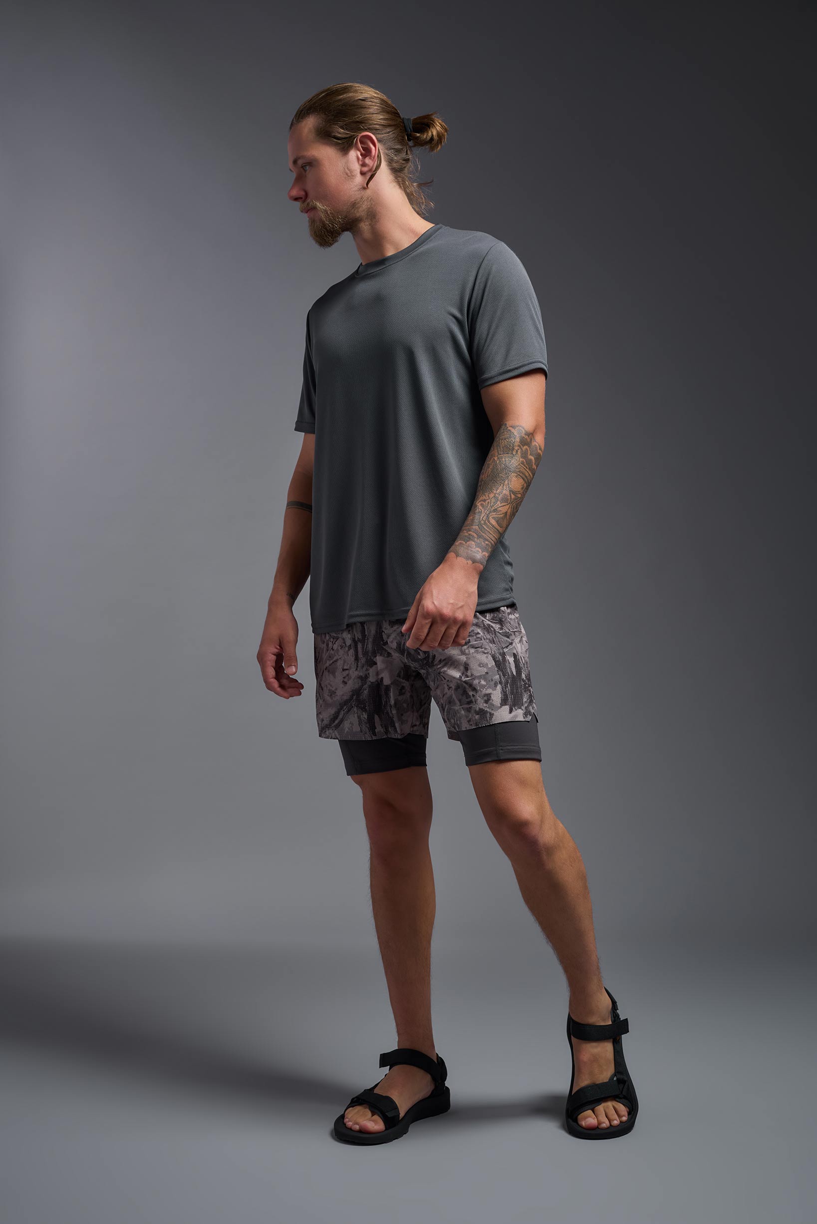 A male model wearing the men's Oxymesh Long Sleeve Tech Tee Imported Version in the color graphite gray, made out of 100% polyester, showing the relaxed fit from a side view. This shirt is breathable, quick-drying, moisture-wicking, and Imported for a better price on bulk apparel. #graphite-gray