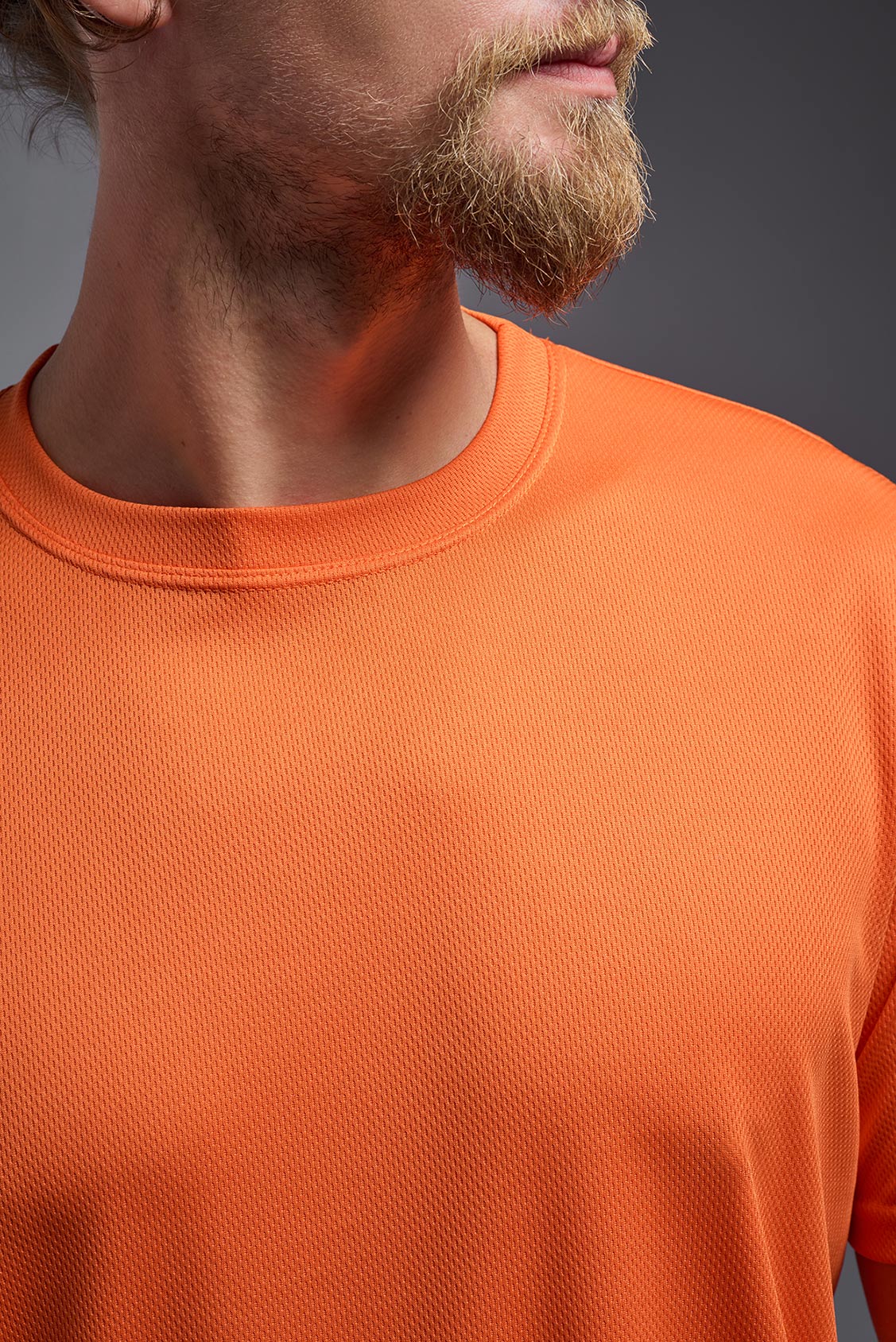 A male model wearing the men's Oxymesh Long Sleeve Tech Tee Imported Version in the color orange, made out of 100% polyester, showing the relaxed fit from a close-up collar view. This shirt is breathable, quick-drying, moisture-wicking, and Imported for a better price on bulk apparel. #orange