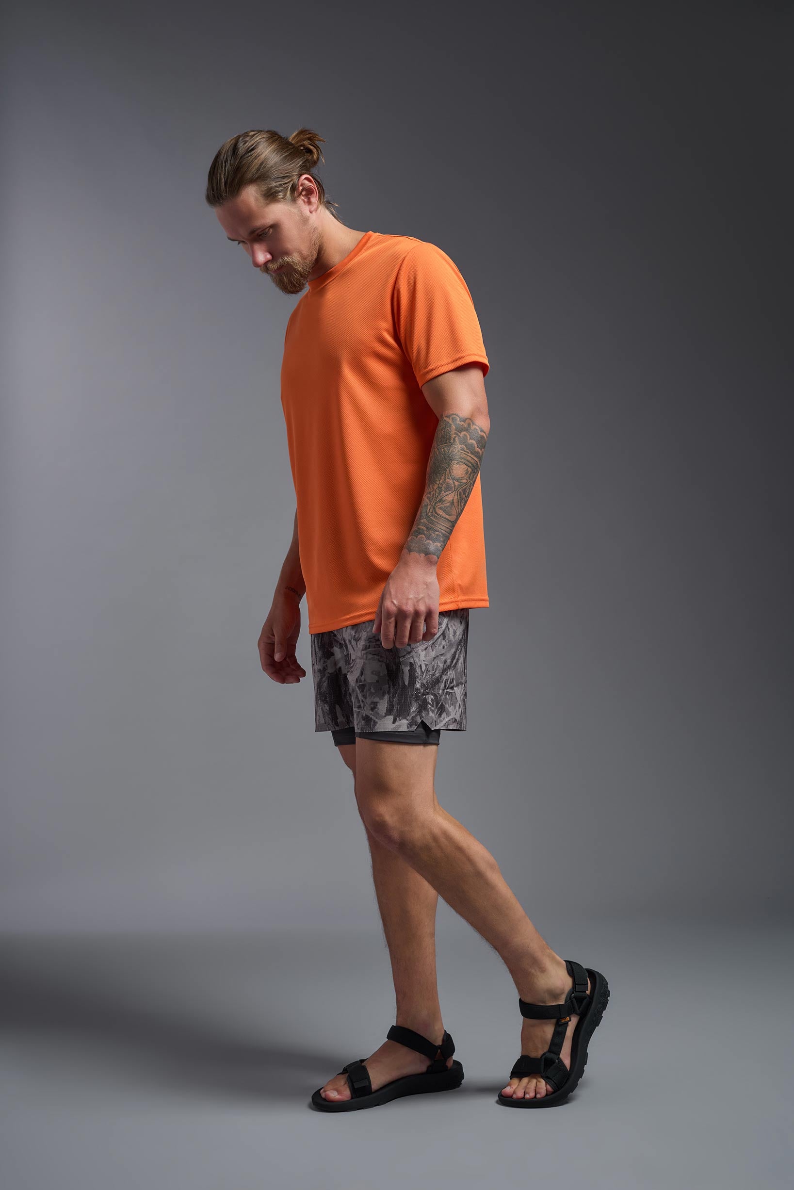 A male model wearing the men's Oxymesh Long Sleeve Tech Tee Imported Version in the color orange, made out of 100% polyester, showing the relaxed fit from a side view. This shirt is breathable, quick-drying, moisture-wicking, and Imported for a better price on bulk apparel. #orange