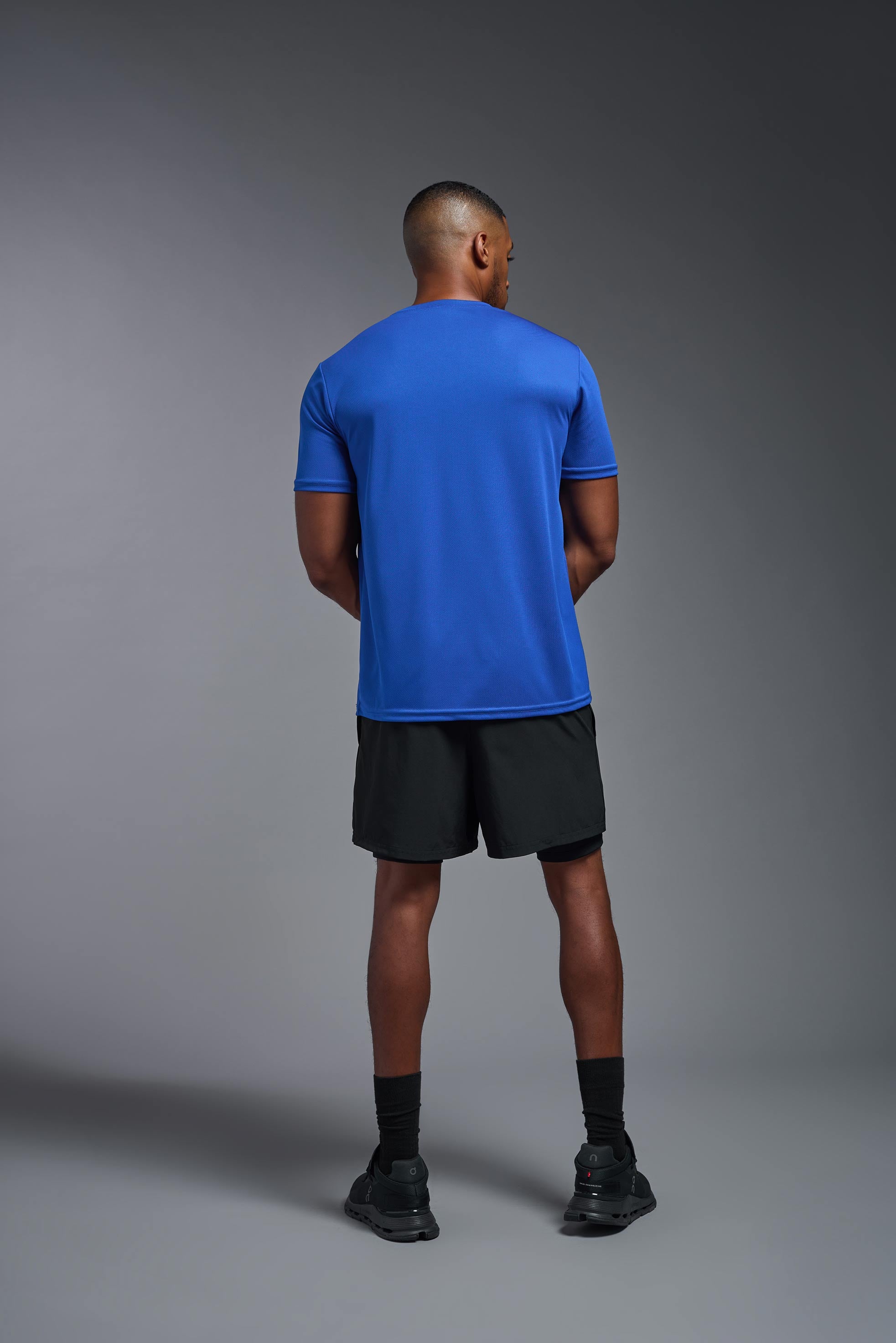A male model wearing the men's Oxymesh Long Sleeve Tech Tee Imported Version in the color royal blue, made out of 100% polyester, showing the relaxed fit from a back view. This shirt is breathable, quick-drying, moisture-wicking, and Imported for a better price on bulk apparel. #royal-blue
