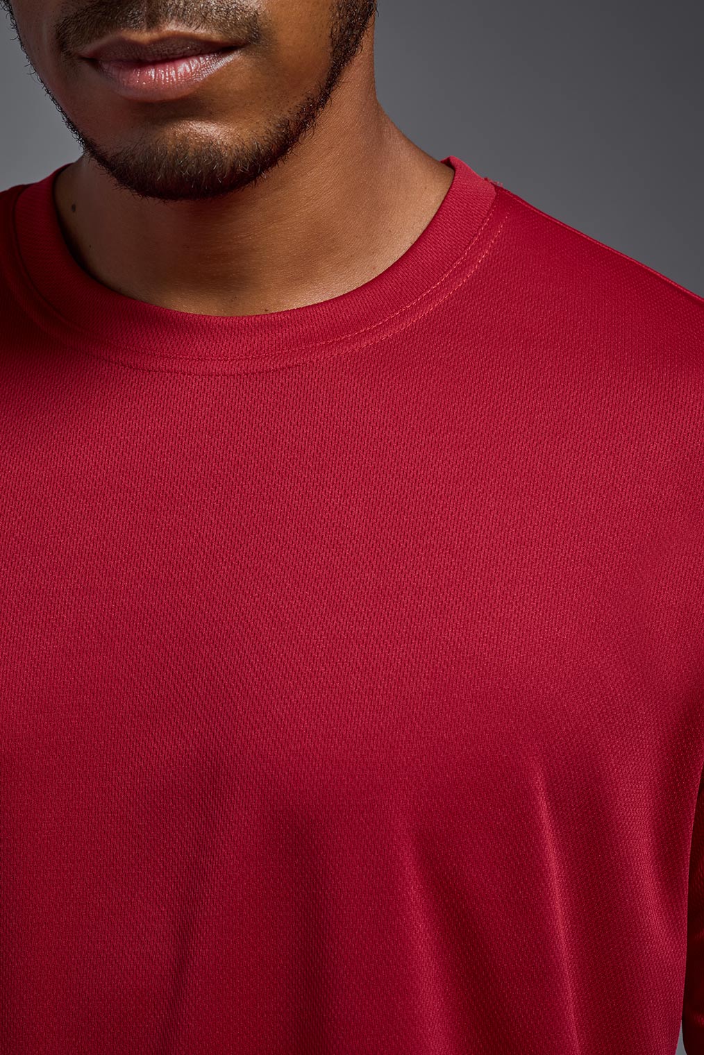 A male model wearing the men's Oxymesh Short Sleeve Tech Tee Imported Version in the color true red, made out of 100% polyester, showing the relaxed fit from a close-up collar view. This shirt is breathable, quick-drying, moisture-wicking, and Imported for a better price on bulk apparel. #true-red