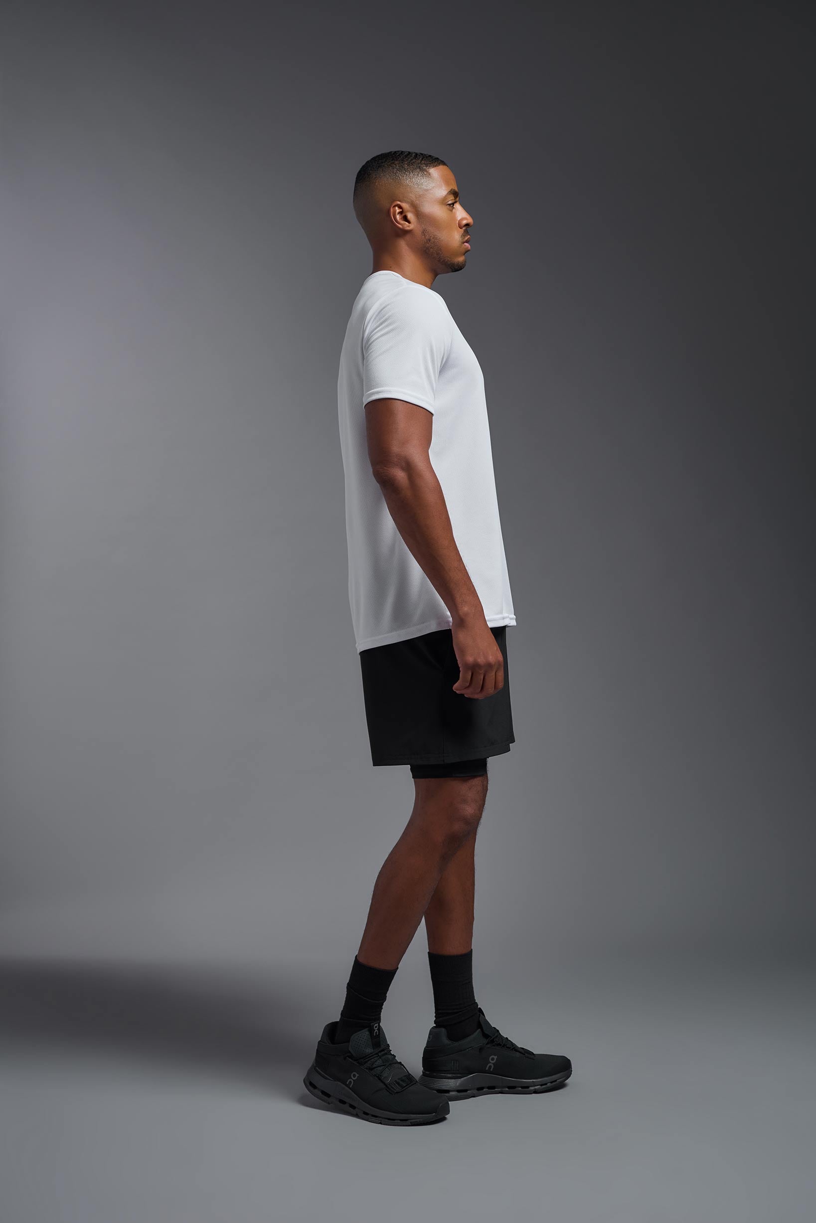 A male model wearing the men's Oxymesh Crewneck Tech Tee Imported Version in the color white, made out of 100% polyester, showing the relaxed fit from a side view. This shirt is breathable, quick-drying, moisture-wicking, and Imported for a better price on bulk apparel. #white