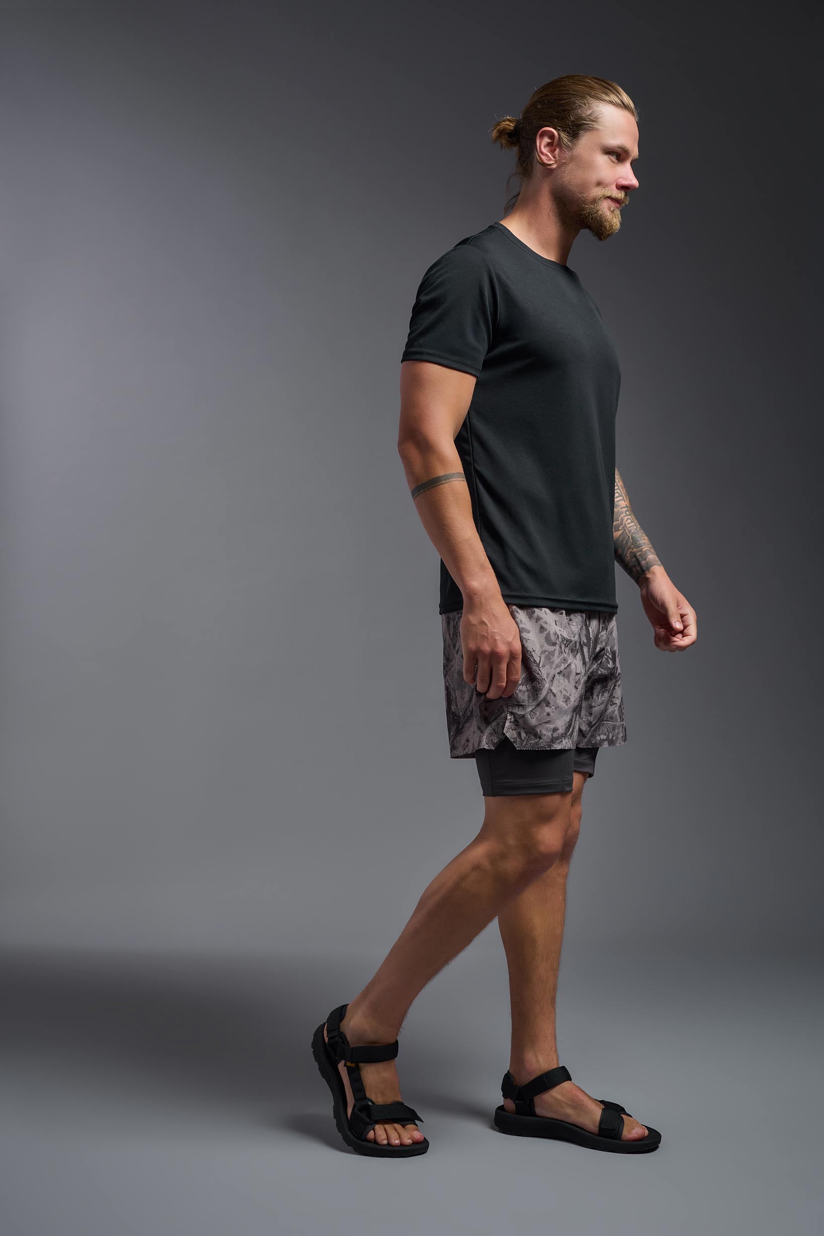 A male model wearing the men's Oxymesh Crewneck Tech Tee in the color black, made out of 100% polyester, showing the relaxed fit from a side view. This shirt is breathable, wicks away moisture, quick-dries, and is made in the USA. #black