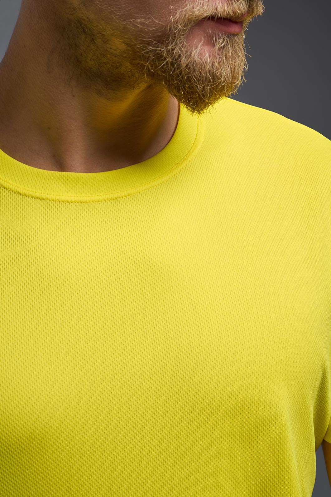 A male model wearing the men's Oxymesh Crewneck Tech Tee in the color bright yellow, made out of 100% polyester, showing the relaxed fit from a front collar close-up view. This shirt is breathable, wicks away moisture, quick-dries, and is made in the USA. #bright-yellow