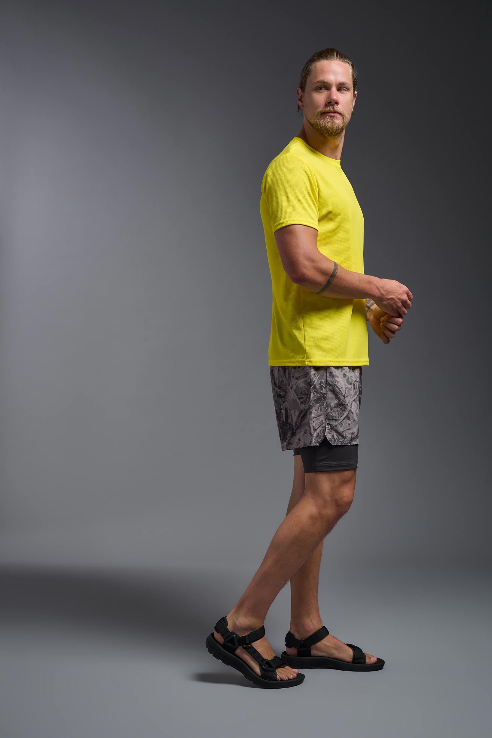 A male model wearing the men's Oxymesh Crewneck Tech Tee in the color bright yellow, made out of 100% polyester, showing the relaxed fit from a side view. This shirt is breathable, wicks away moisture, quick-dries, and is made in the USA. #bright-yellow
