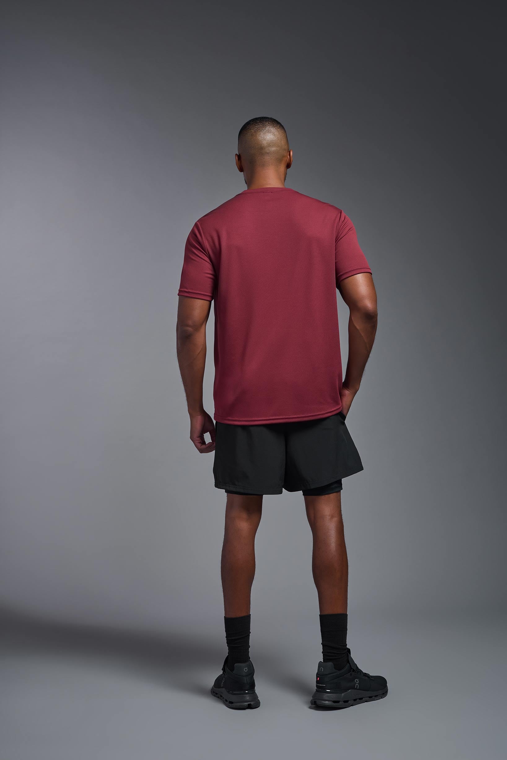 A male model wearing the men's Oxymesh Crewneck Tech Tee in the color cardinal made out of 100% polyester, showing the relaxed fit from a back view. This shirt is breathable, wicks away moisture, quick-dries, and is made in the USA. #cardinal
