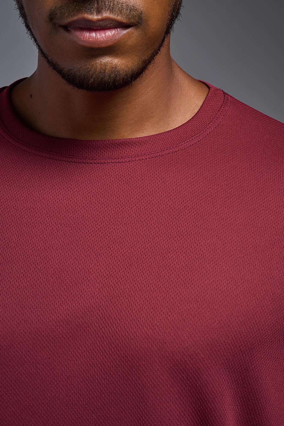 A male model wearing the men's Oxymesh Crewneck Tech Tee in the color cardinal made out of 100% polyester, showing the relaxed fit from a front collar close-up view. This shirt is breathable, wicks away moisture, quick-dries, and is made in the USA. #cardinal