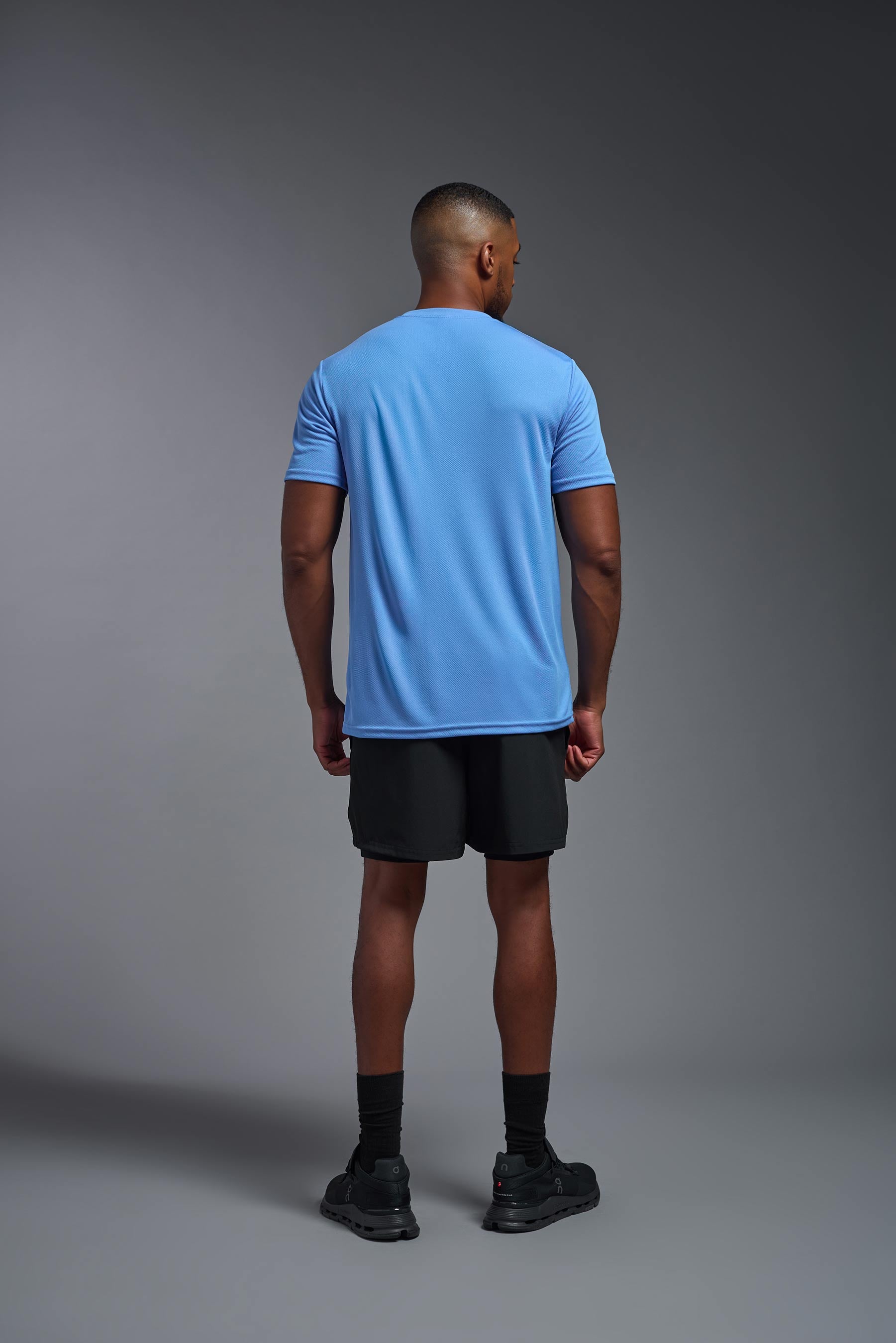 A male model wearing the men's Oxymesh Crewneck Tech Tee in the color carolina blue made out of 100% polyester, showing the relaxed fit from a back view. This shirt is breathable, wicks away moisture, quick-dries, and is made in the USA. #carolina-blue