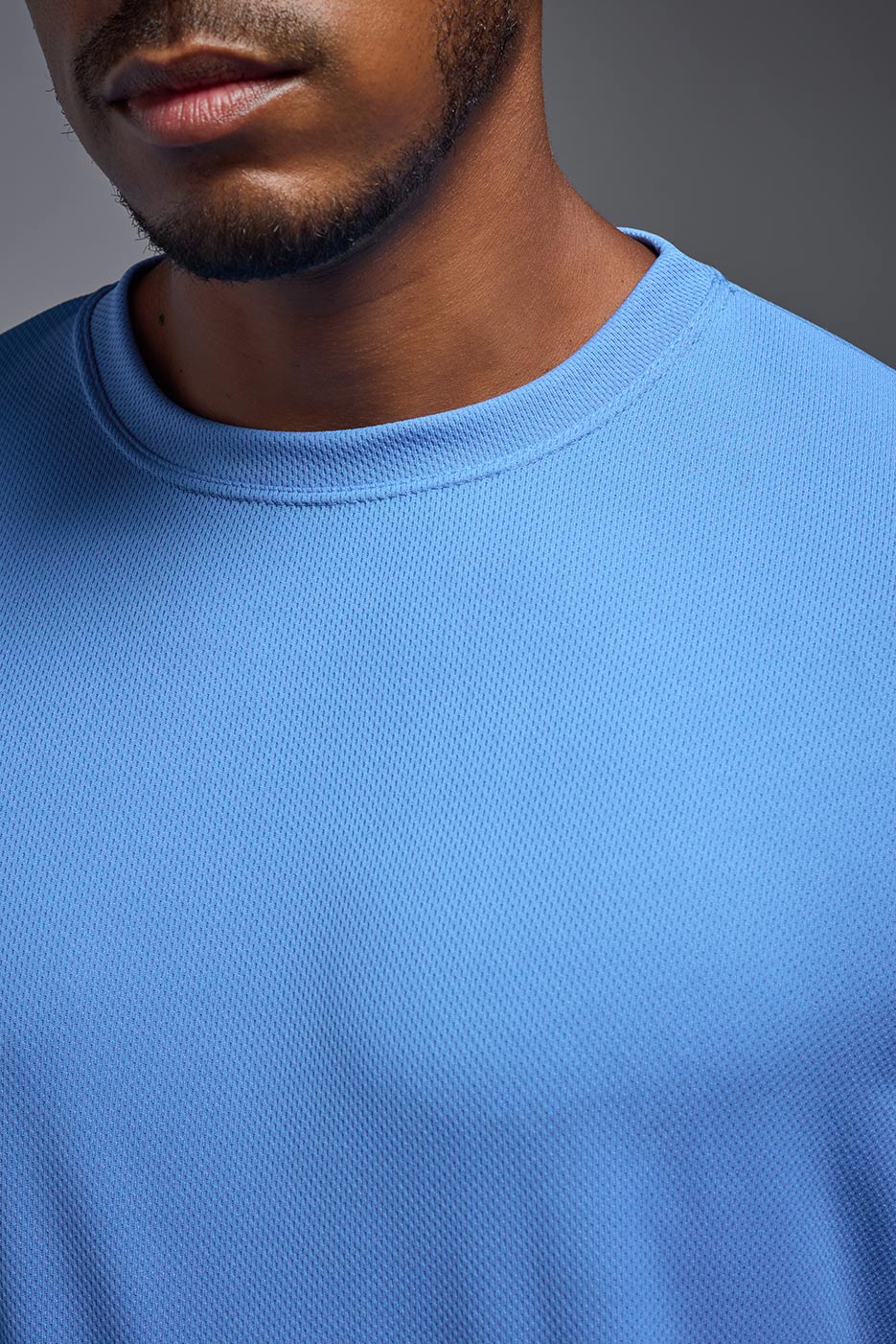 A male model wearing the men's Oxymesh Crewneck Tech Tee in the color carolina blue made out of 100% polyester, showing the relaxed fit from a close-up collar view. This shirt is breathable, wicks away moisture, quick-dries, and is made in the USA. #carolina-blue