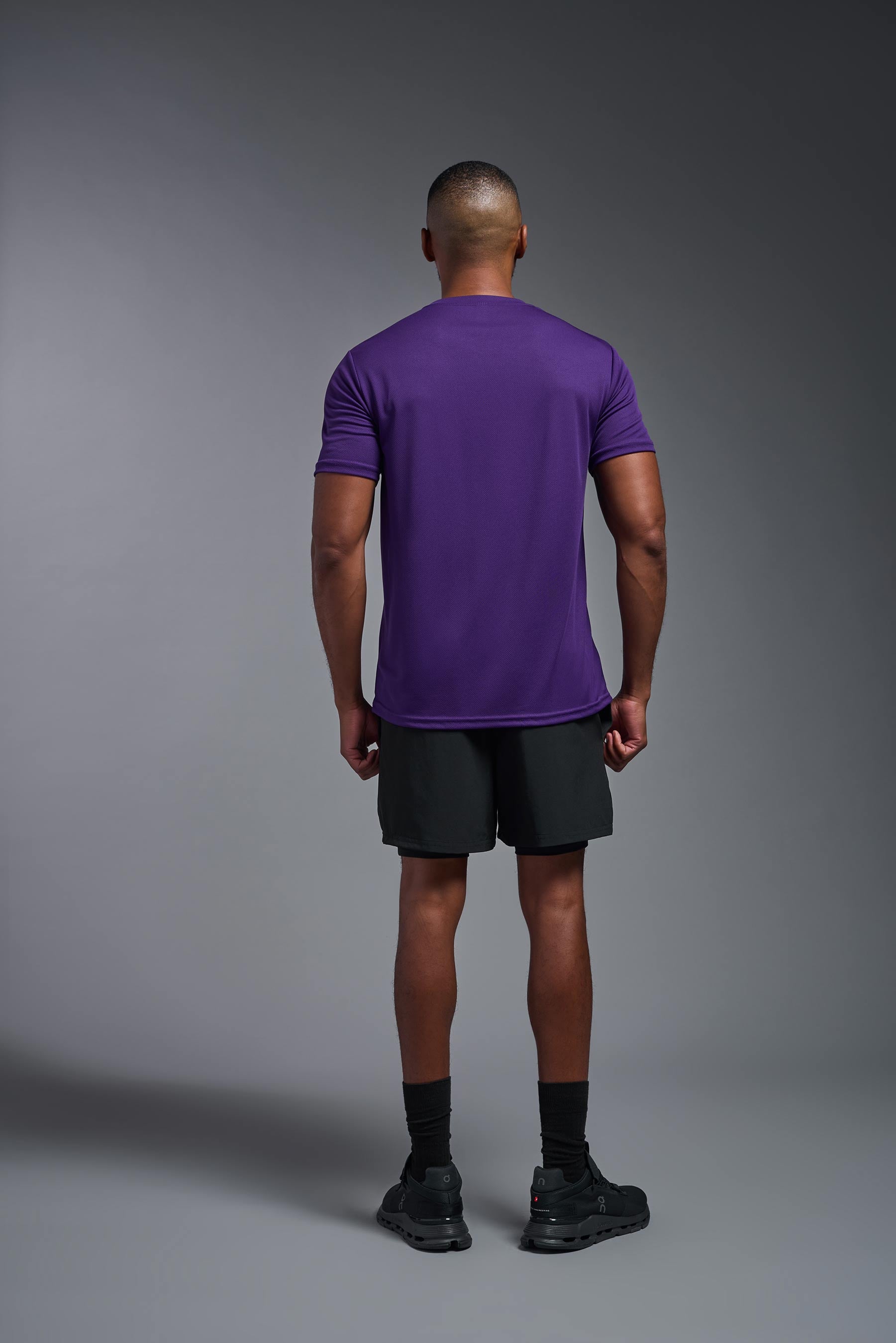 A male model wearing the men's Oxymesh Crewneck Tech Tee in the color dark purple made out of 100% polyester, showing the relaxed fit from a back view. This shirt is breathable, wicks away moisture, quick-dries, and is made in the USA. #dark-purple