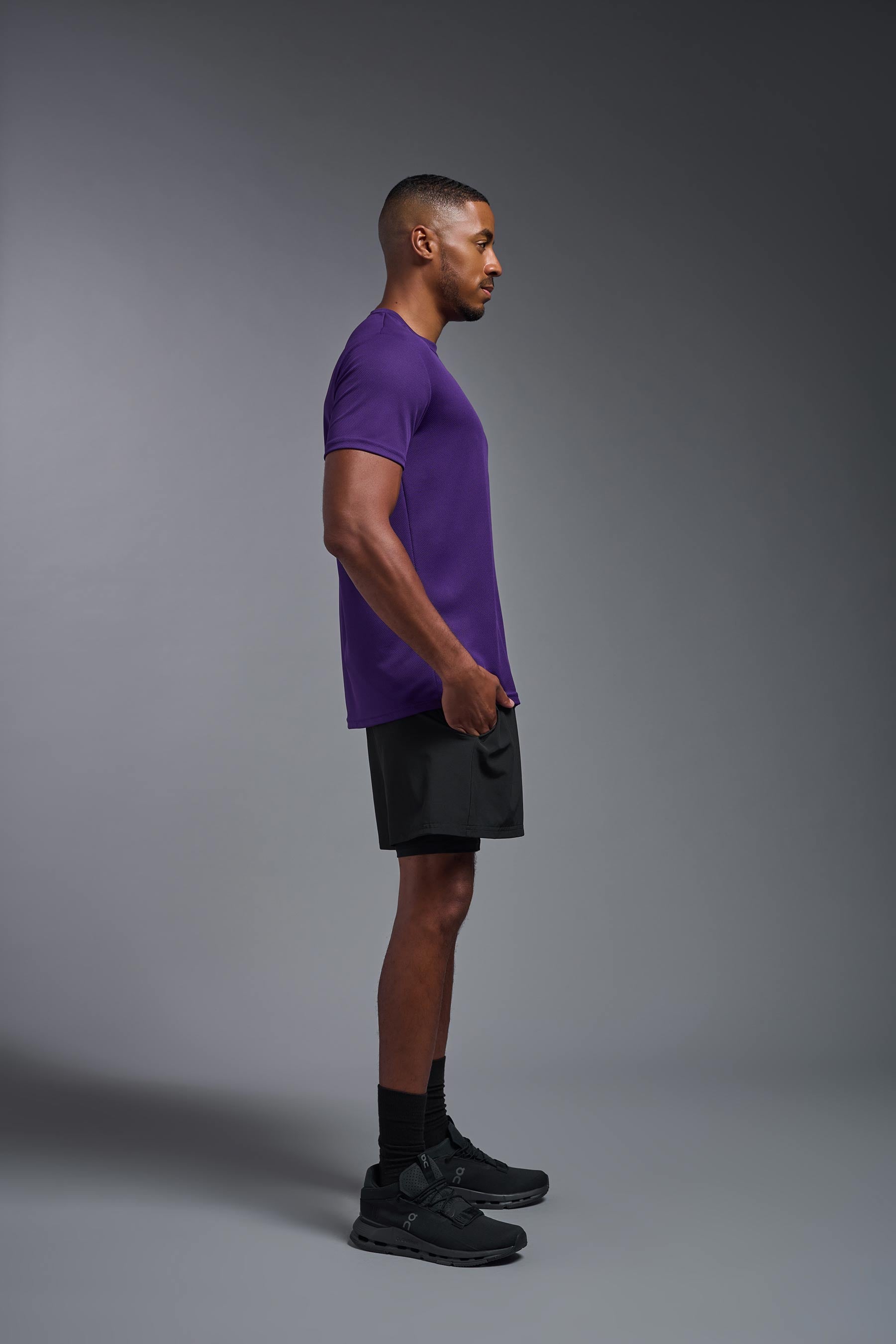 A male model wearing the men's Oxymesh Crewneck Tech Tee in the color dark purple made out of 100% polyester, showing the relaxed fit from a side view. This shirt is breathable, wicks away moisture, quick-dries, and is made in the USA. #dark-purple