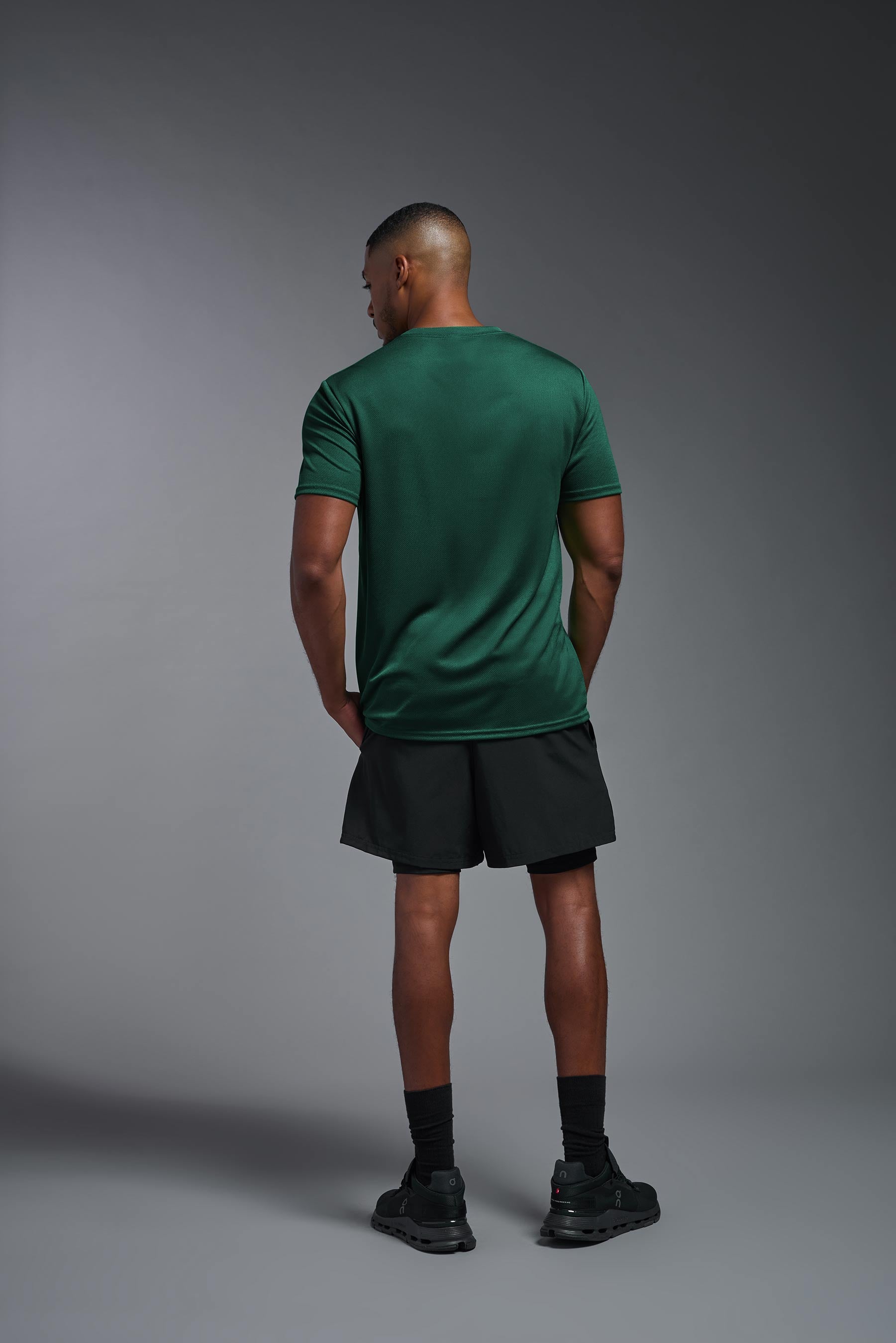 A male model wearing the men's Oxymesh Crewneck Tech Tee in the color forest green made out of 100% polyester, showing the relaxed fit from a back view. This shirt is breathable, wicks away moisture, quick-dries, and is made in the USA. #forest-green
