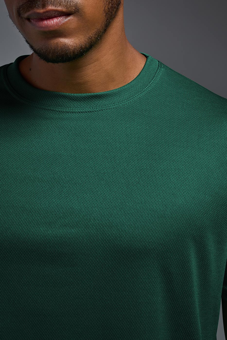 A male model wearing the men's Oxymesh Crewneck Tech Tee in the color forest green made out of 100% polyester, showing the relaxed fit from a front close-up collar view. This shirt is breathable, wicks away moisture, quick-dries, and is made in the USA. #forest-green