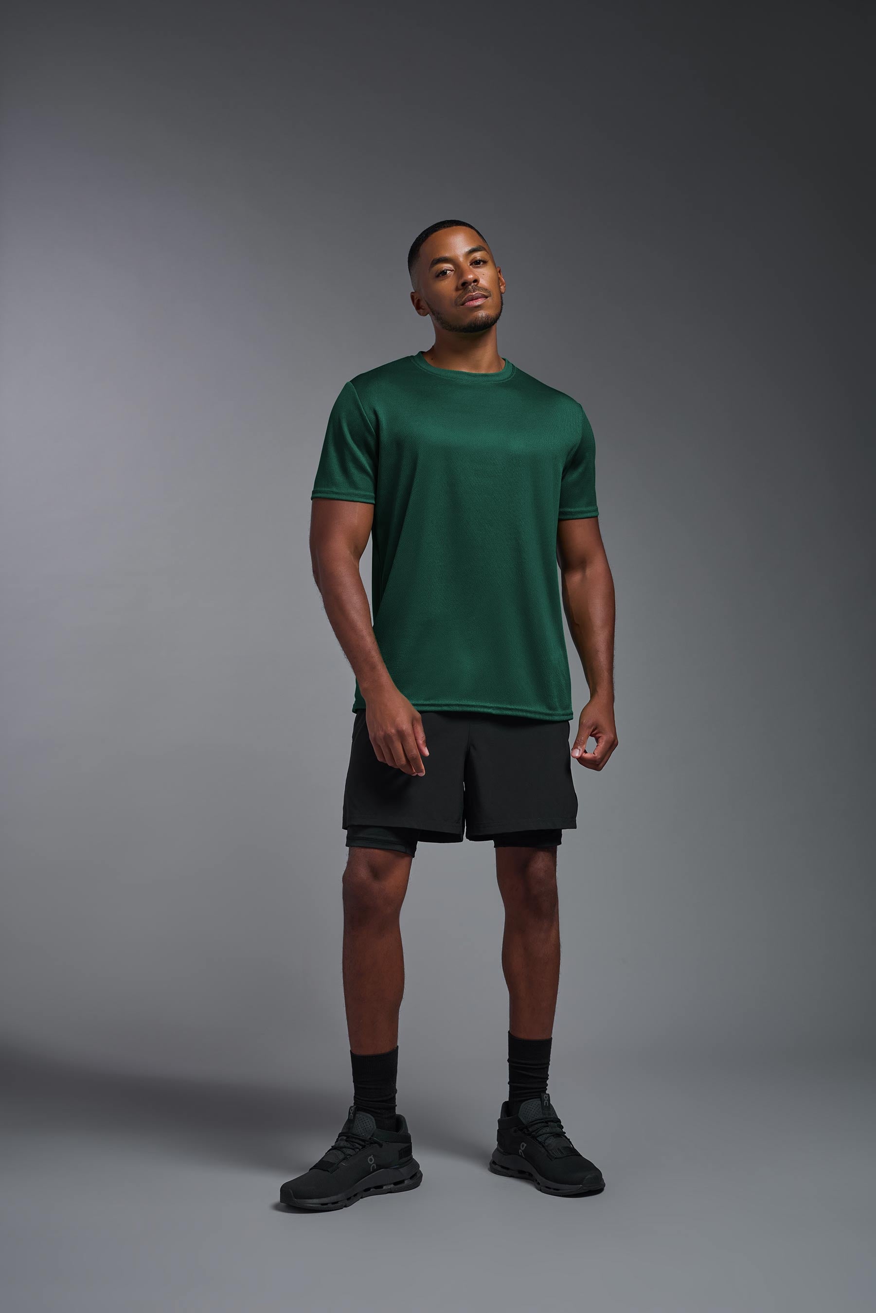 A male model wearing the men's Oxymesh Crewneck Tech Tee in the color forest green made out of 100% polyester, showing the relaxed fit from a front view. This shirt is breathable, wicks away moisture, quick-dries, and is made in the USA. #forest-green