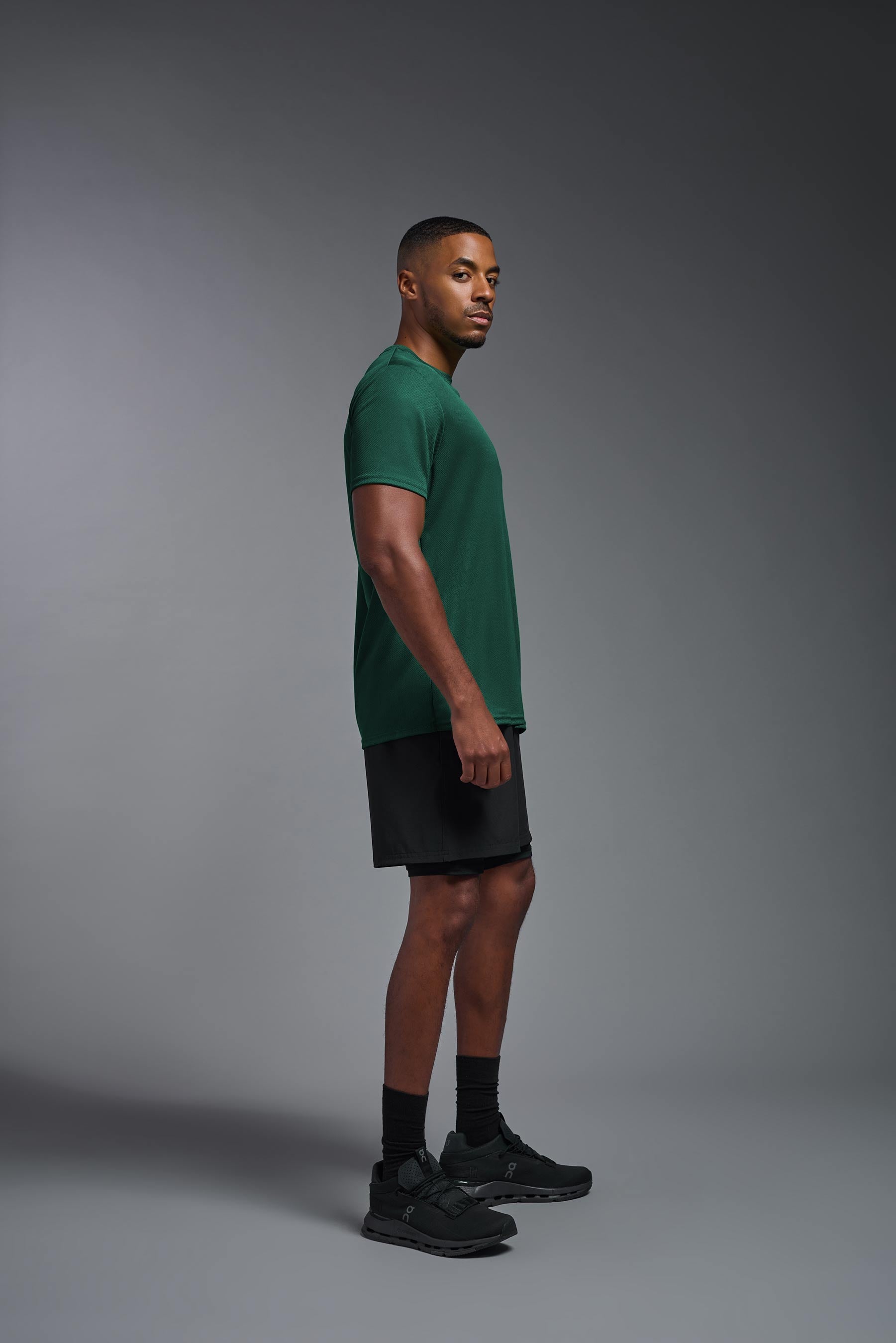 A male model wearing the men's Oxymesh Crewneck Tech Tee in the color forest green made out of 100% polyester, showing the relaxed fit from a side view. This shirt is breathable, wicks away moisture, quick-dries, and is made in the USA. #forest-green