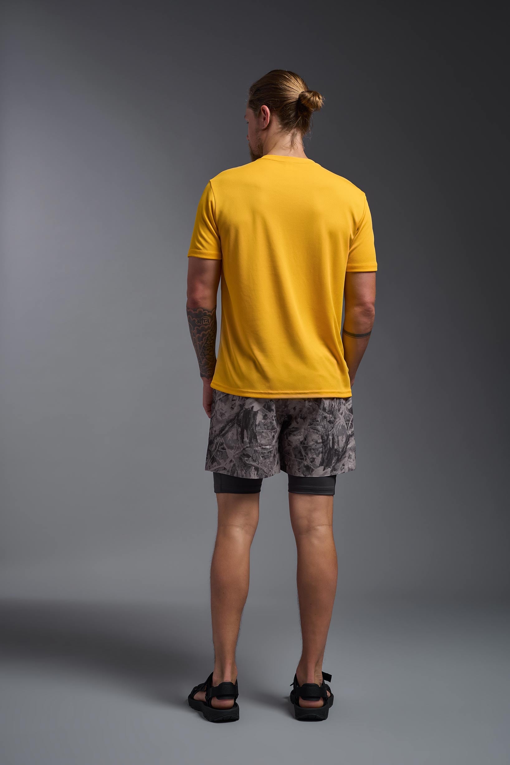 A male model wearing the men's Oxymesh Crewneck Tech Tee in the color gold, made out of 100% polyester, showing the relaxed fit from a back view. This shirt is breathable, wicks away moisture, quick-dries, and is made in the USA. #gold