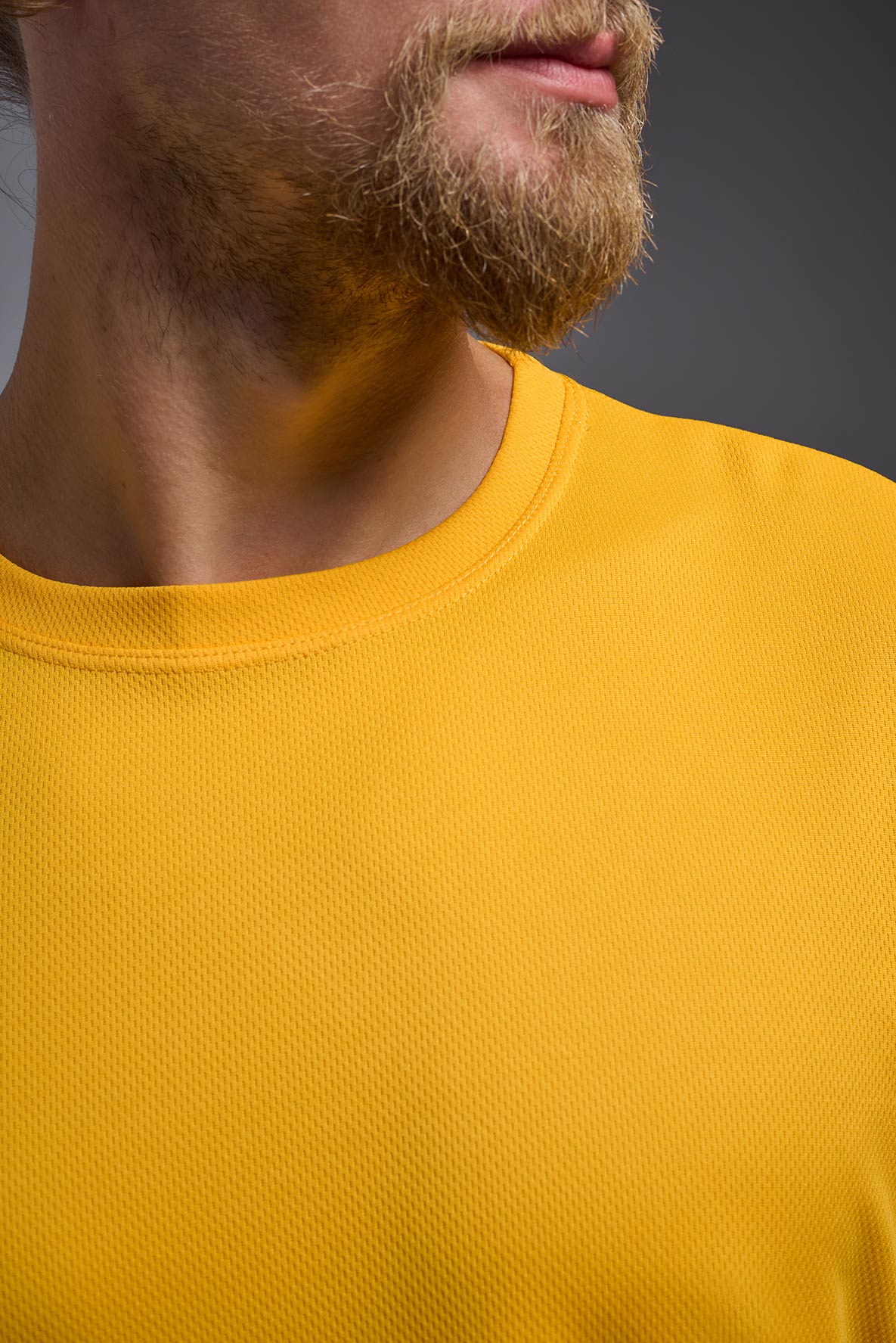A male model wearing the men's Oxymesh Crewneck Tech Tee in the color gold, made out of 100% polyester, showing the relaxed fit from a front collar close-up view. This shirt is breathable, wicks away moisture, quick-dries, and is made in the USA. #gold