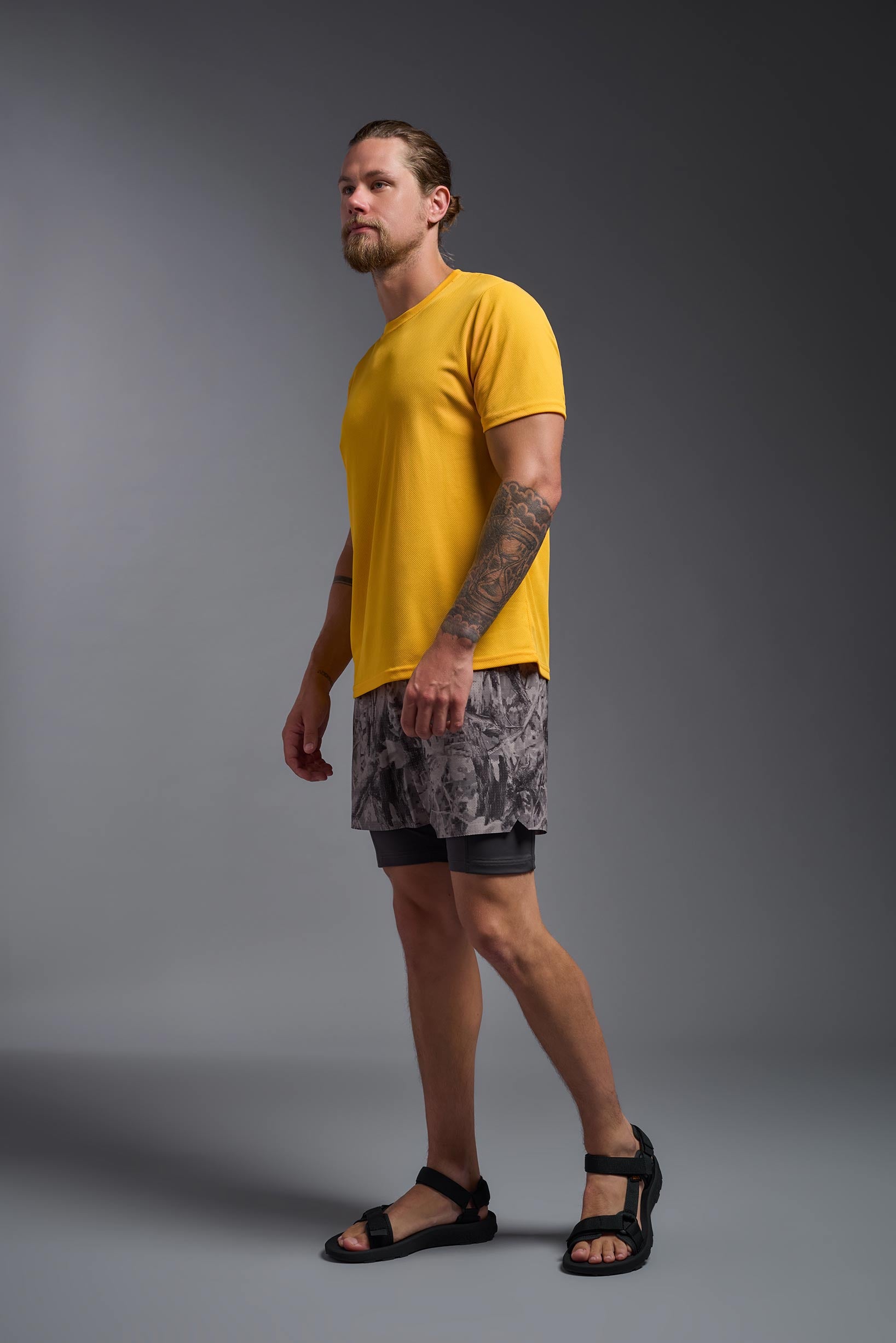 A male model wearing the men's Oxymesh Crewneck Tech Tee in the color gold, made out of 100% polyester, showing the relaxed fit from a full body side view. This shirt is breathable, wicks away moisture, quick-dries, and is made in the USA. #gold