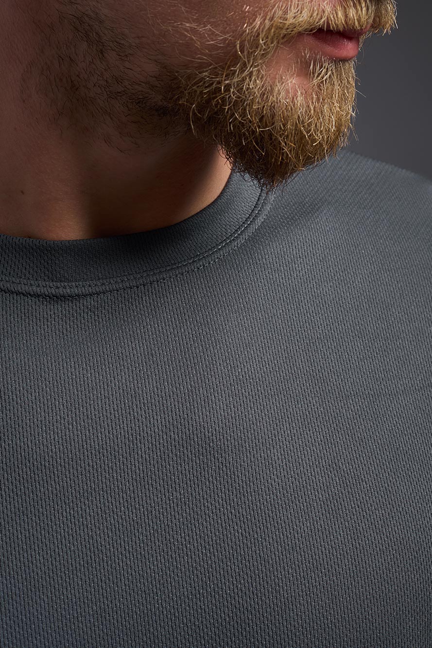 A male model wearing the men's Oxymesh Crewneck Tech Tee in the color graphite gray made out of 100% polyester, showing the relaxed fit from a collar close-up view. This shirt is breathable, wicks away moisture, quick-dries, and is made in the USA. #graphite-gray
