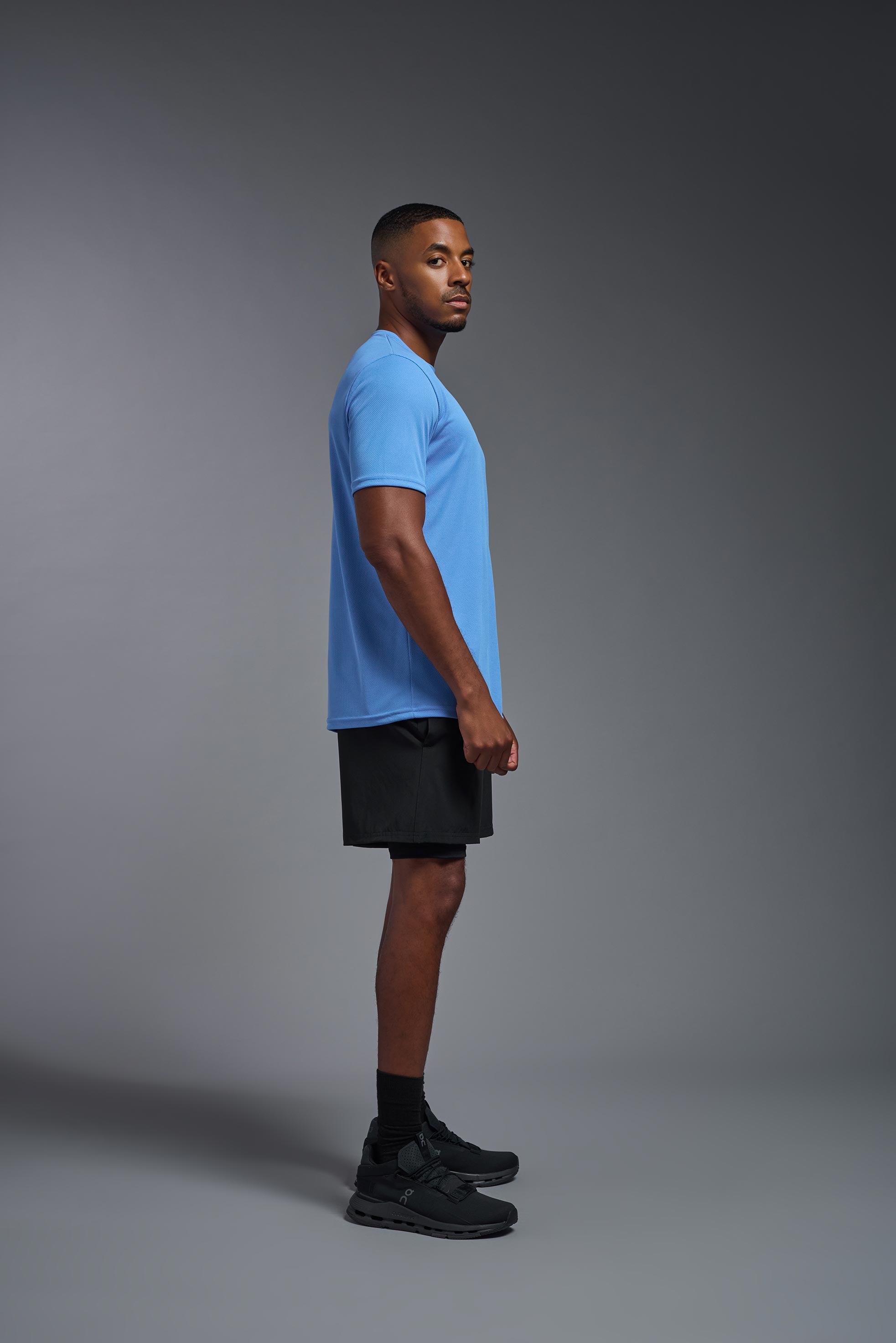 A male model wearing the men's Oxymesh Crewneck Tech Tee Imported Version in the color carolina blue, made out of 100% polyester, showing the relaxed fit from a side view. This shirt is breathable, quick-drying, moisture-wicking, and Imported for a better price on bulk apparel. #carolina-blue